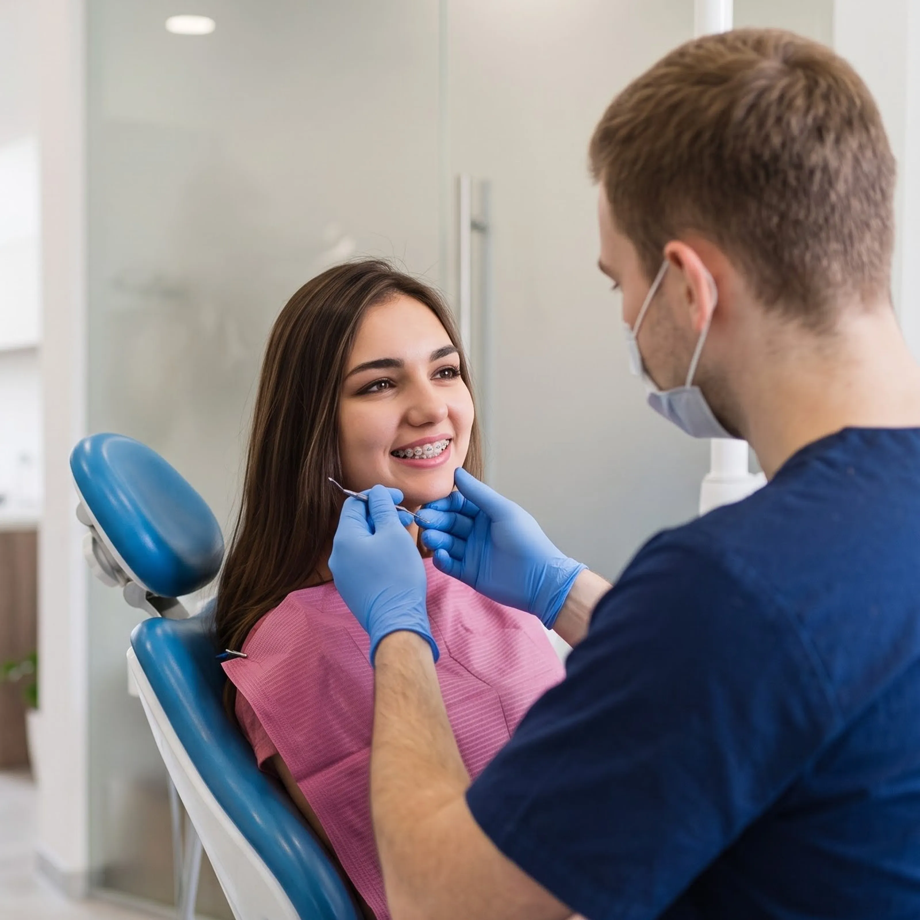 Dentist examining a smiling woman's teeth in a bright orthodontic office