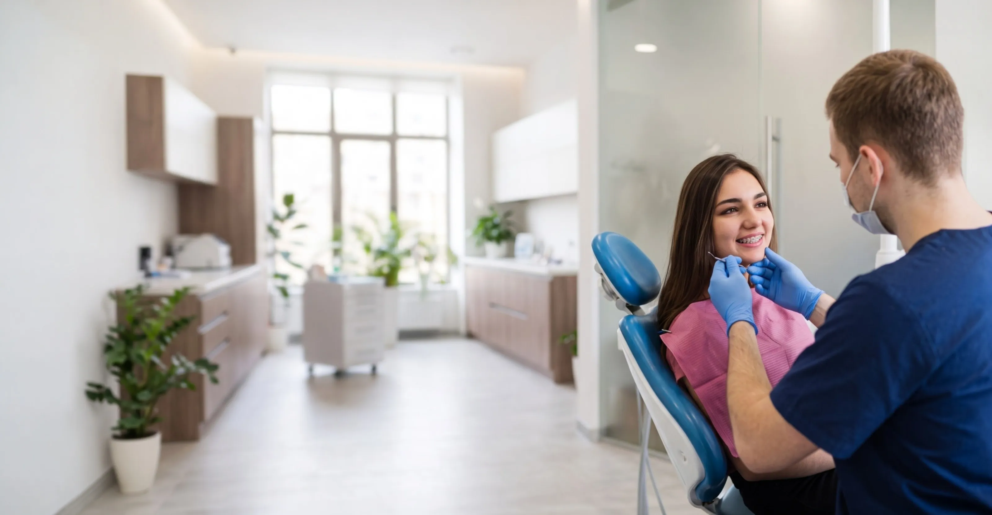 Dentist examining a smiling woman's teeth in a bright orthodontic office