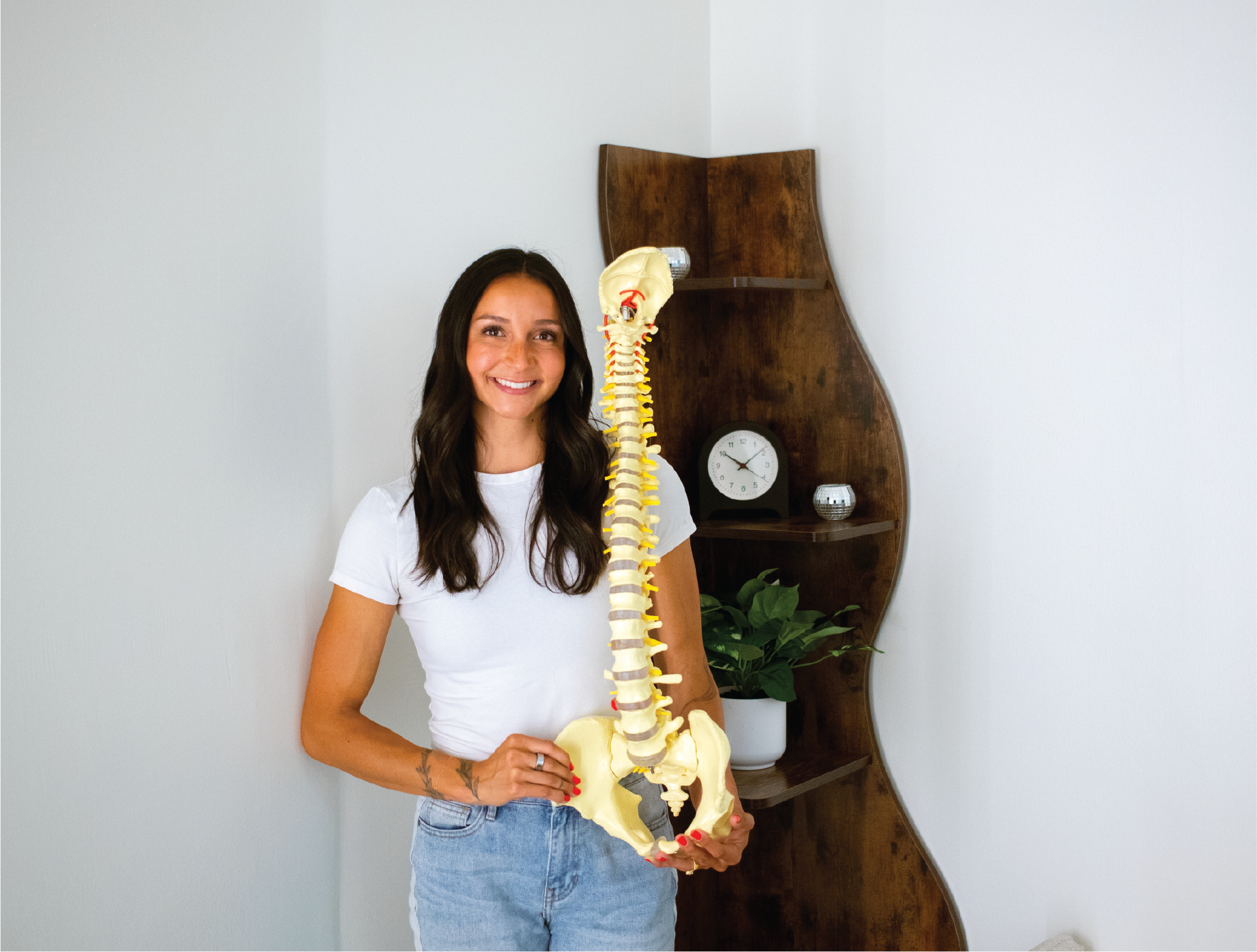 Liv standing in her office with a spine figure, the founder of Liv Well Chiropractic