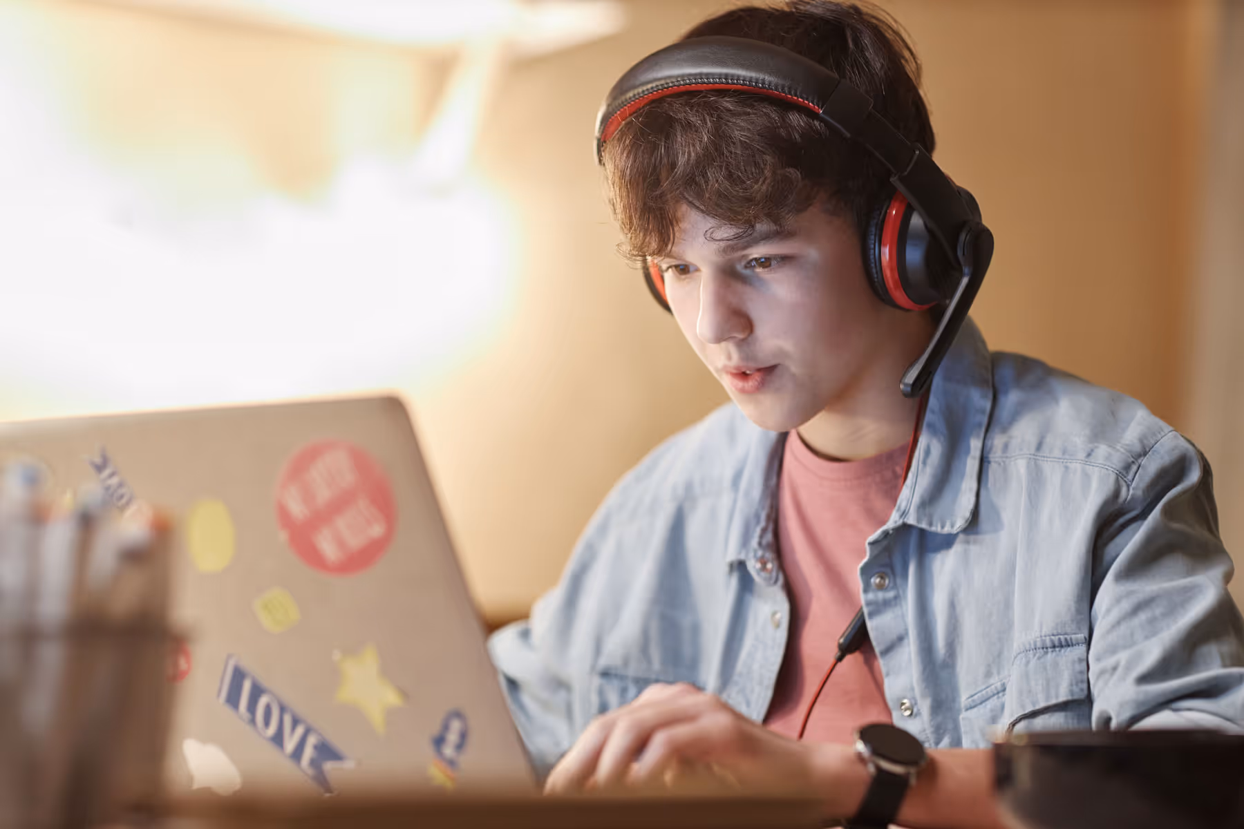 Teenage boy wearing headset and on his laptop at his desk.