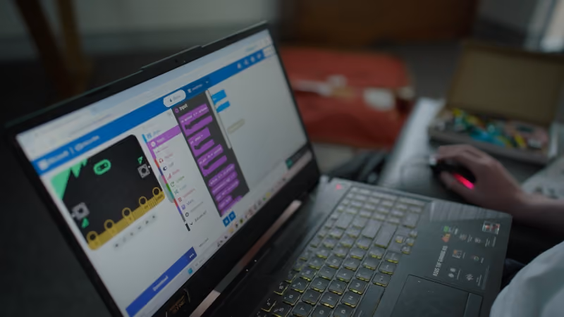 Person coding a game using a block-based programming interface on a laptop.