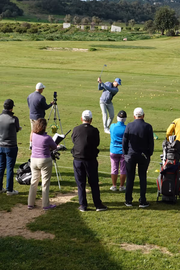 Edward Holland a golf instructor swinging a club while a group of people watch on a green golf course.