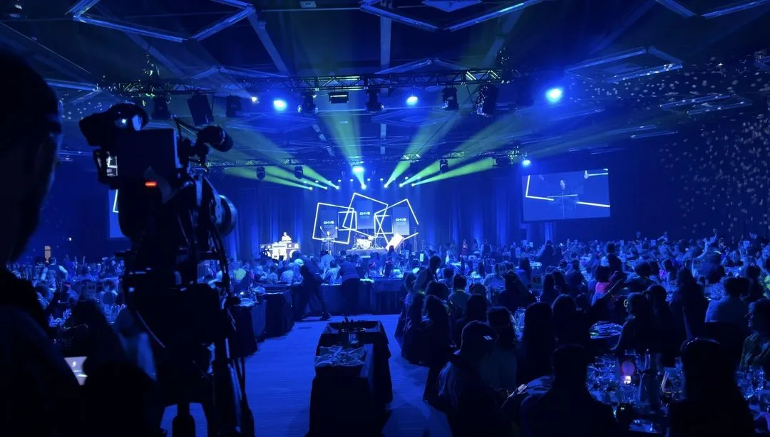 A large group of people are sitting in a dark room with a blue light show.