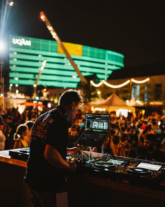 A man is playing music on a laptop at a festival.