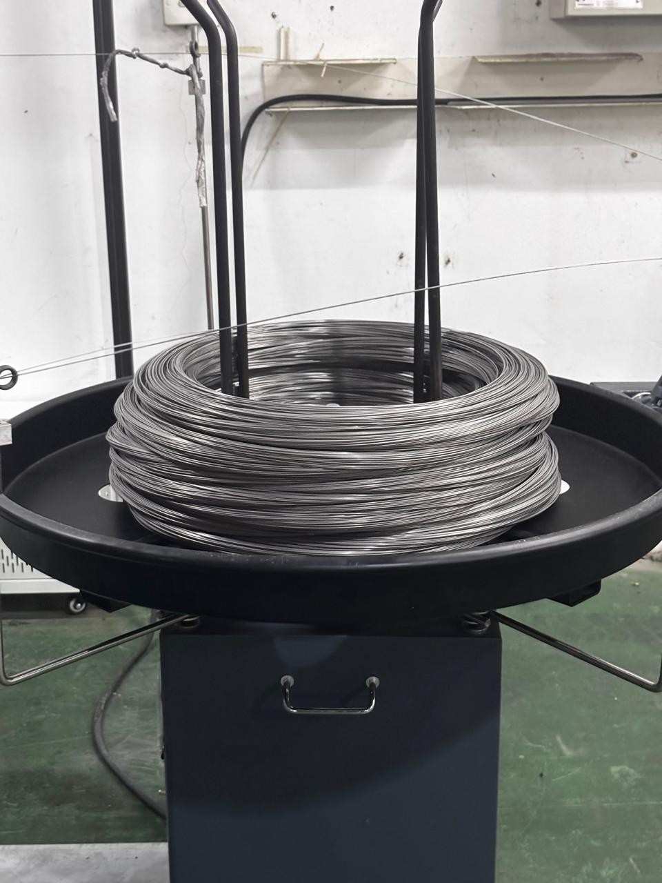 Large coil of metallic wire placed on an industrial spooler machine in a workshop.
