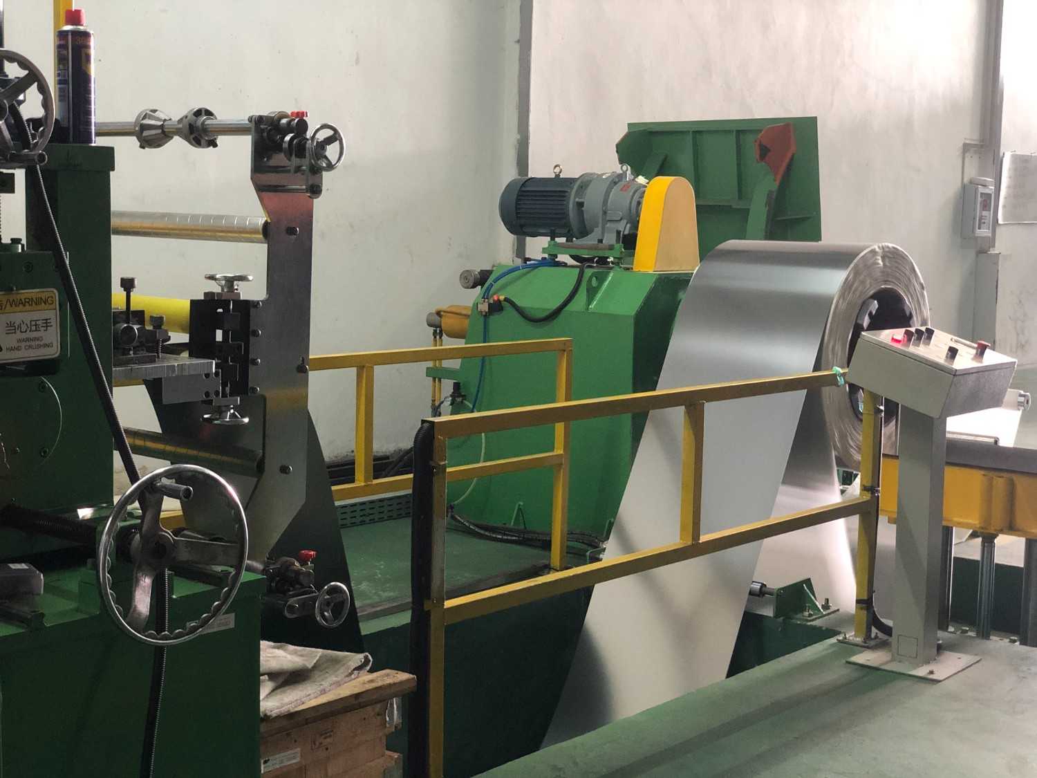 Industrial machinery with a large metal coil being fed through rollers and a control panel nearby.