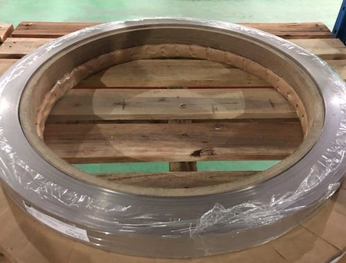 Large metal ring wrapped in plastic resting on a wooden pallet in an industrial setting.