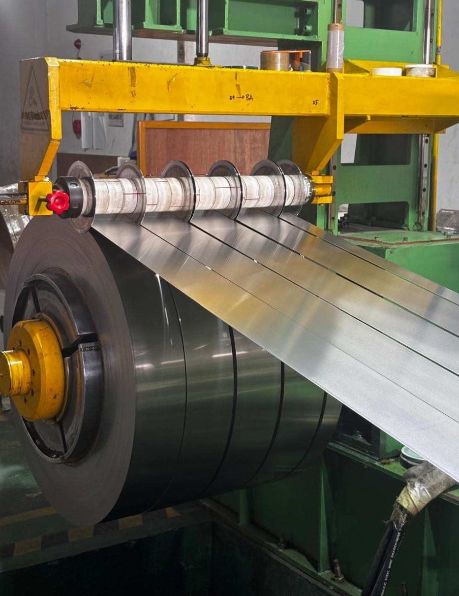 Industrial machine slitting a large roll of metal into several narrower strips.