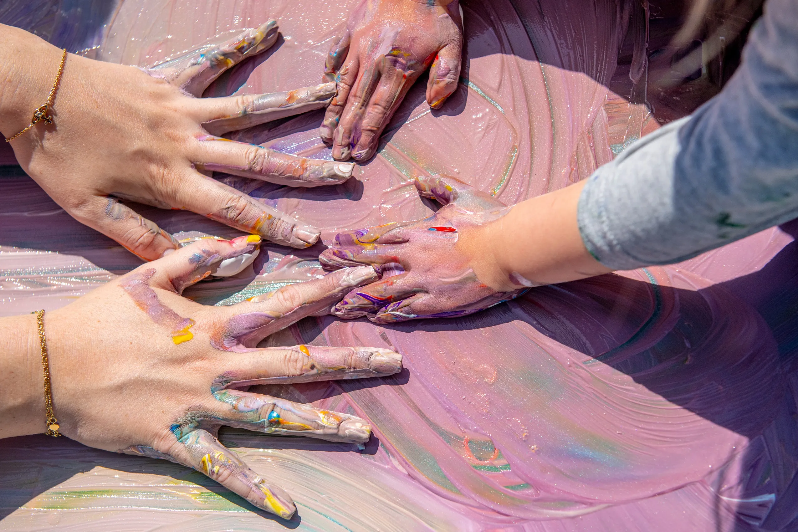 Multiple hands immersed in a pool of swirling pastel-colored paint, conveying tactile exploration and creative expression.