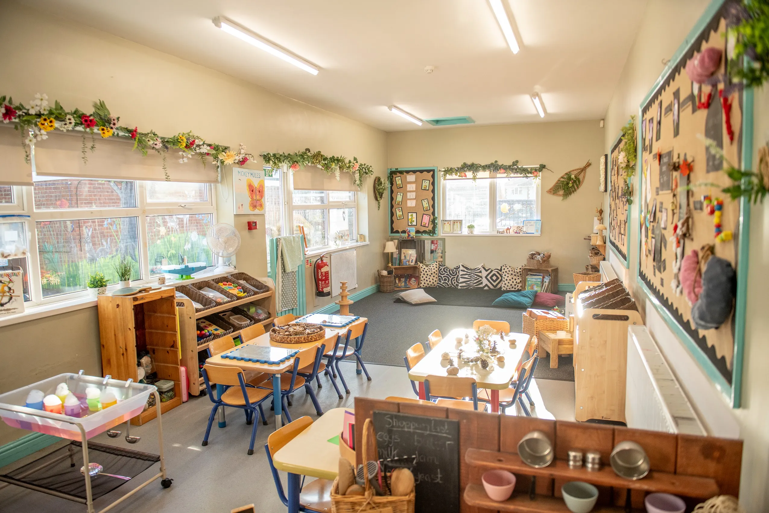 Child-sized wooden tables with blue edges and matching blue and wood chairs, arranged in a classroom setting.