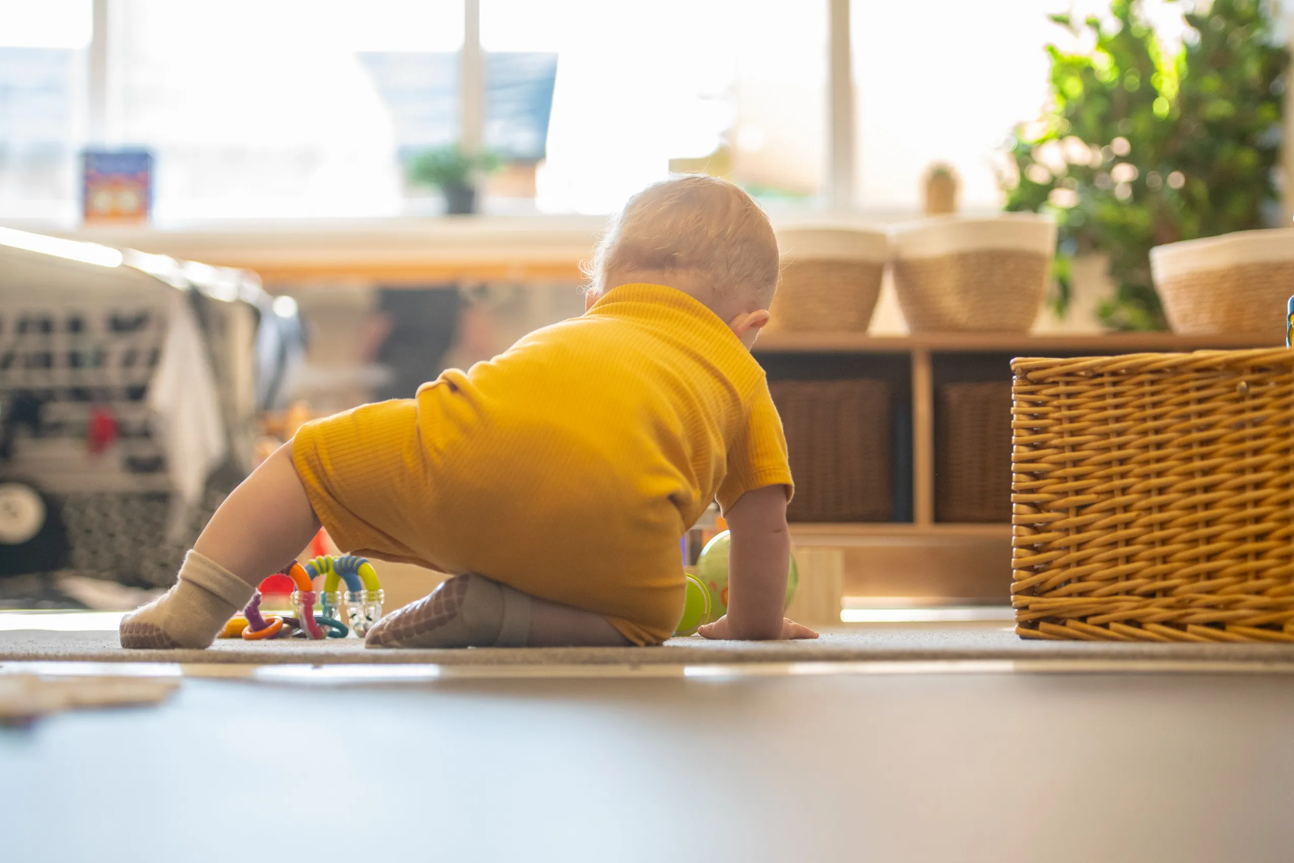 A baby in a yellow outfit on hands and knees on a carpeted floor, with toys nearby.