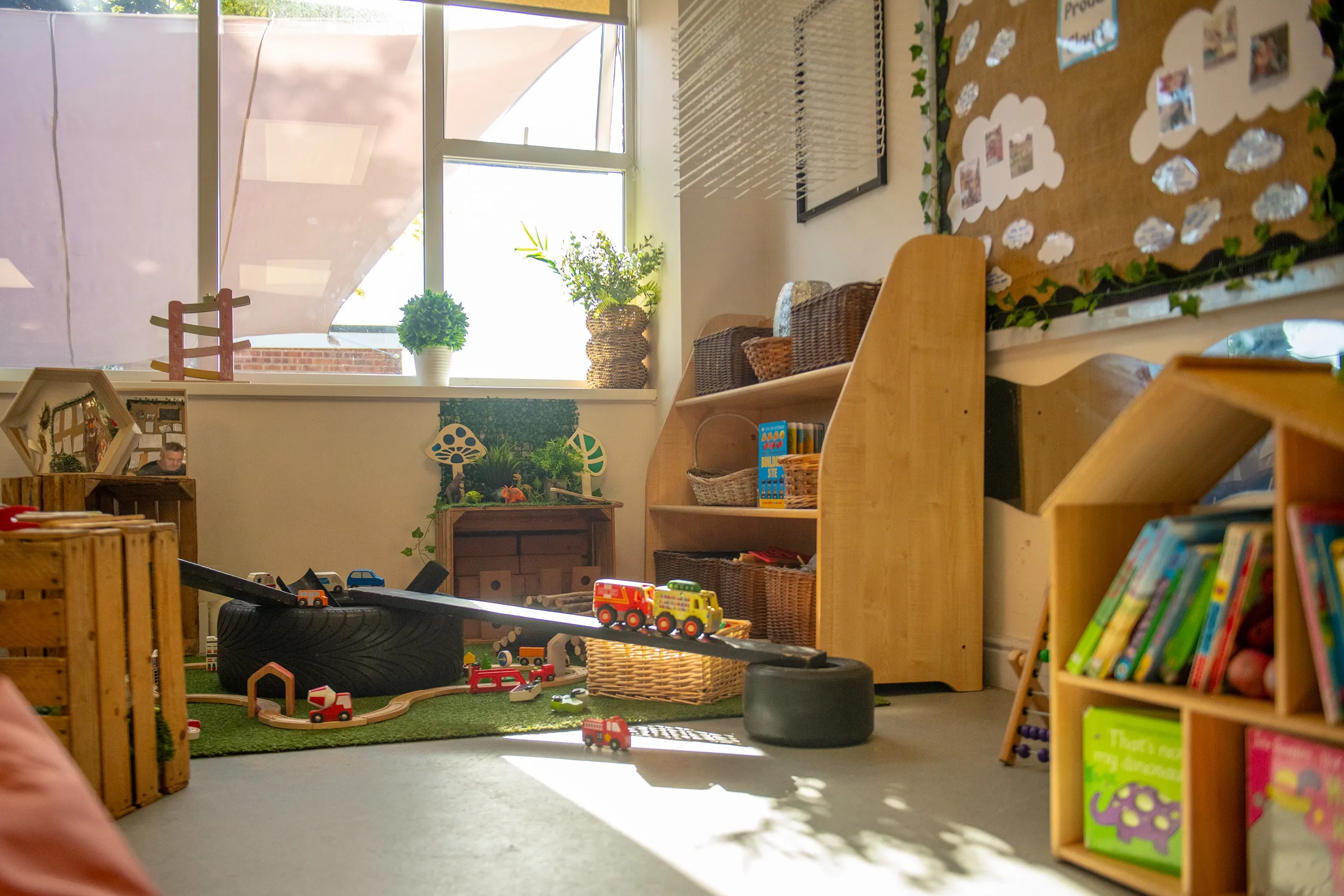 A toy car track with a black ramp, supported by a tire and wooden crate, with toy cars including a fire truck and school bus.