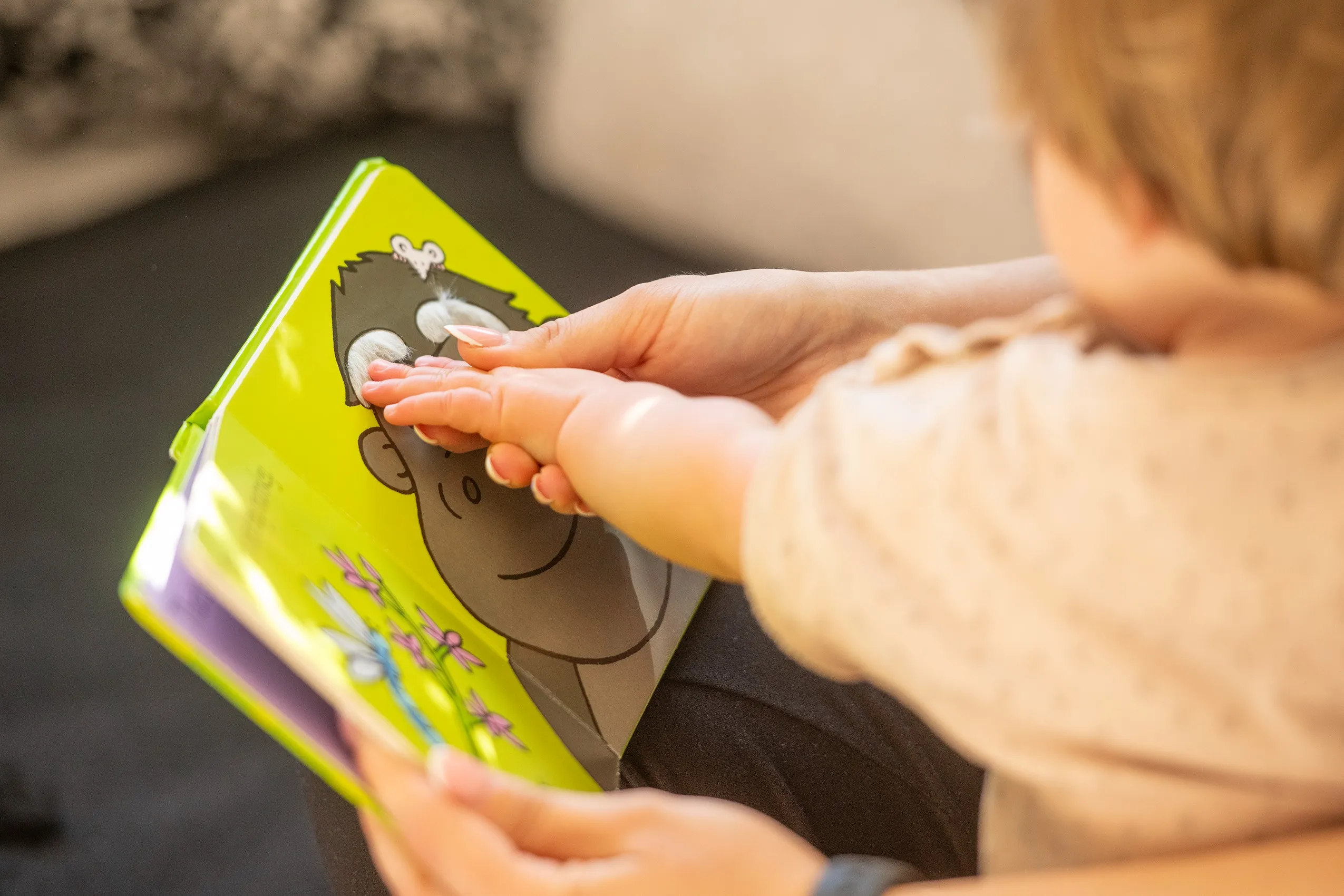A child's hand reaching to touch a cartoon gorilla on the yellow cover of a children's book.