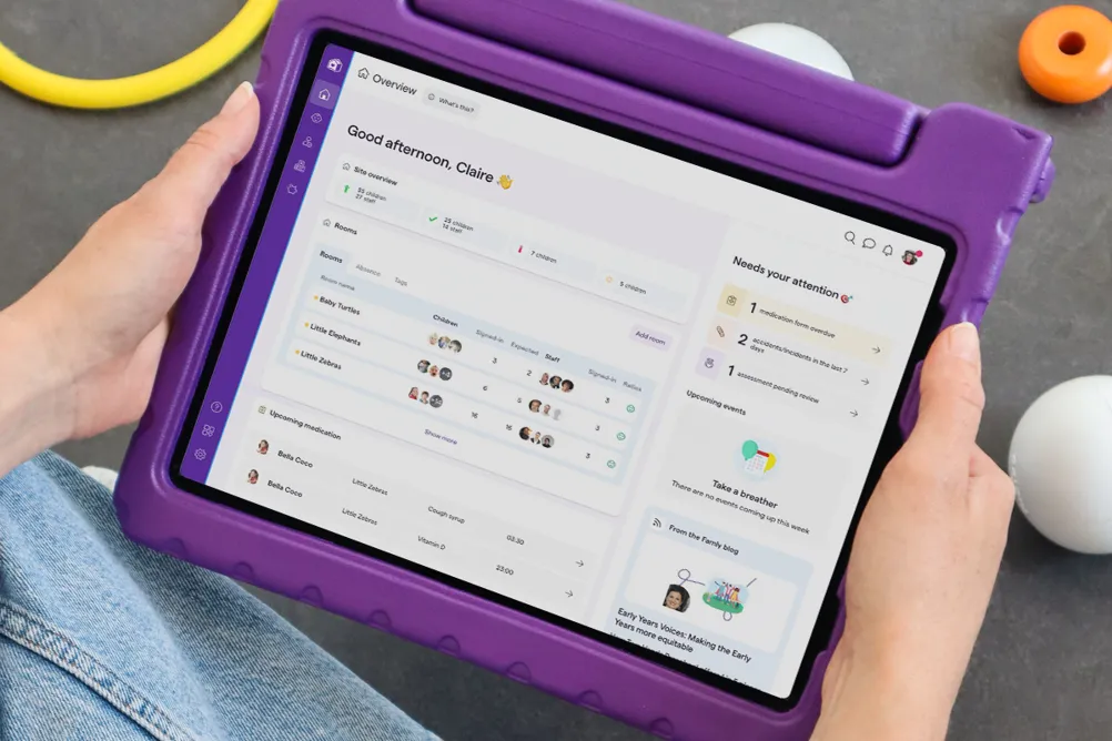 A tablet in a purple case displaying a childcare management interface with site overview, room details, and notifications.