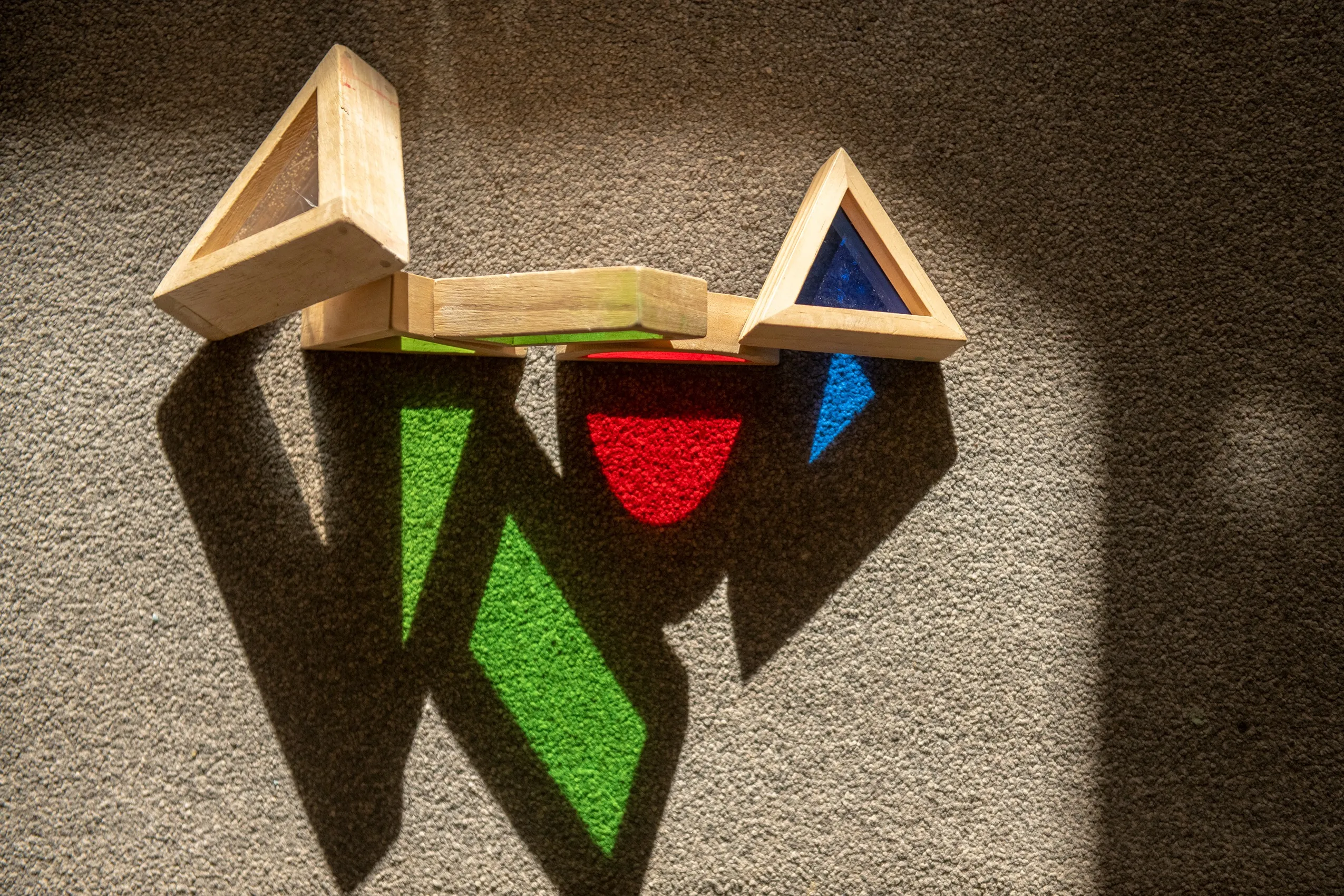 Wooden blocks with colored transparent plastic casting colored shadows on a textured surface.