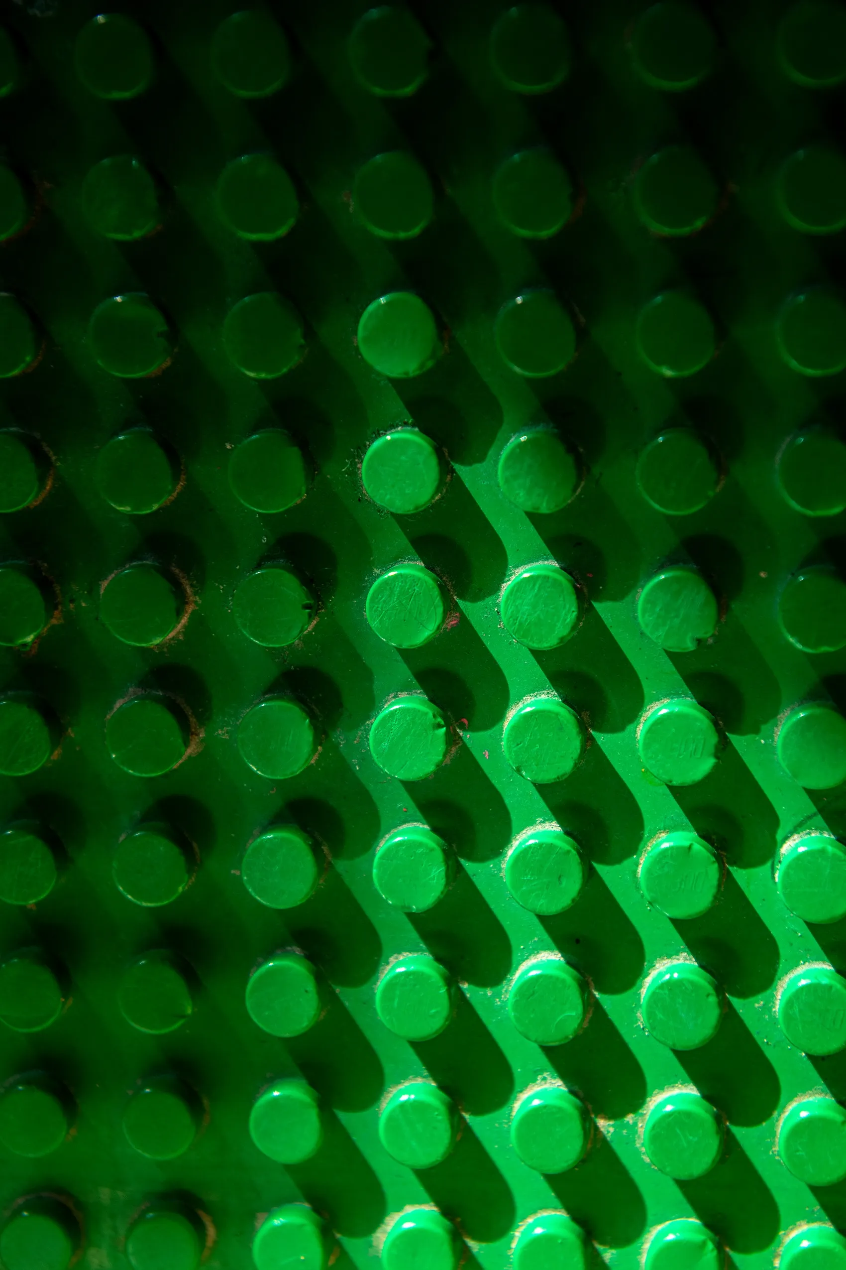 A bright green Lego baseplate with circular studs, partially illuminated.