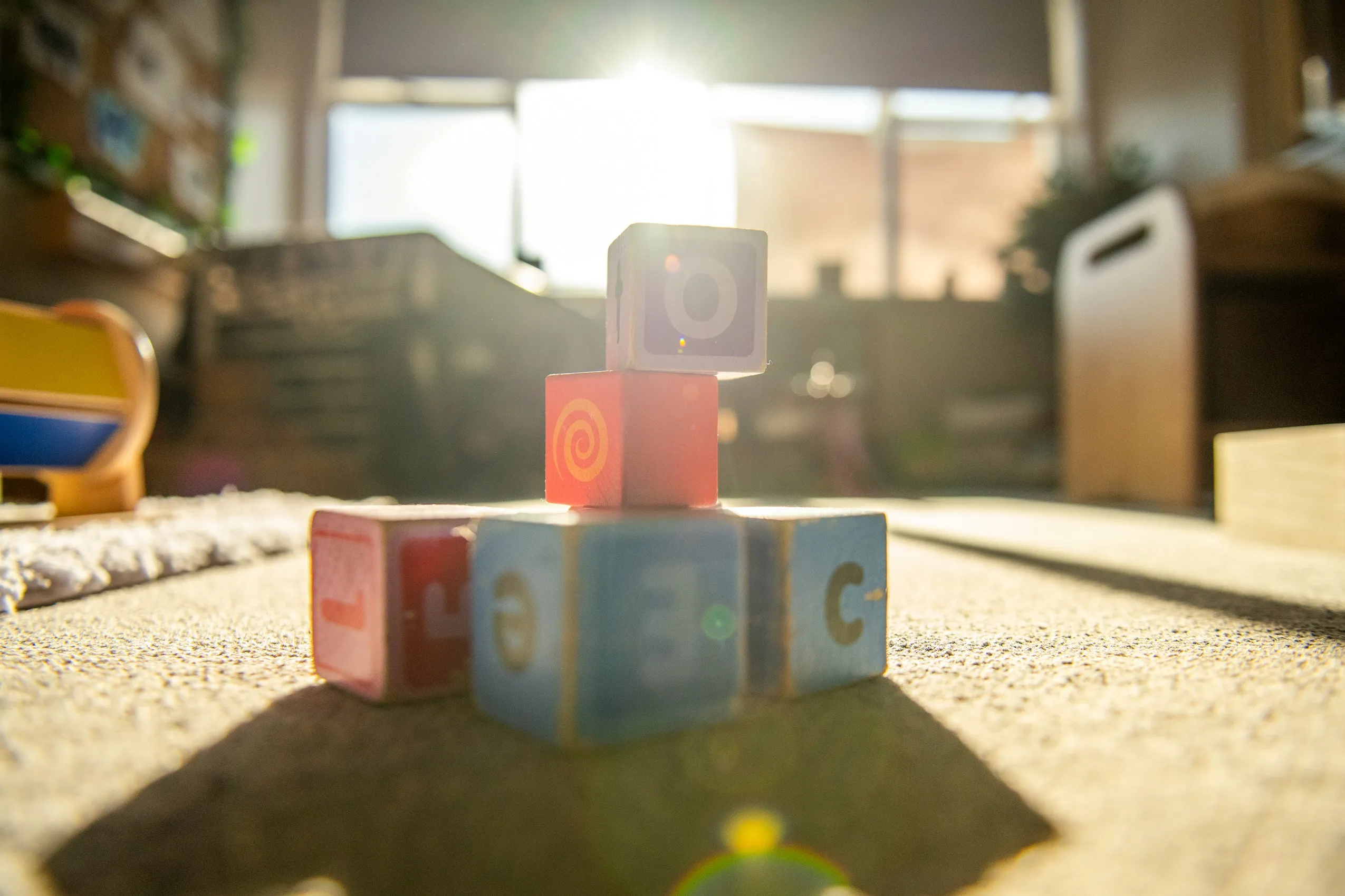 A pyramid stack of five colorful wooden children's blocks with letters and symbols, on a carpeted floor.