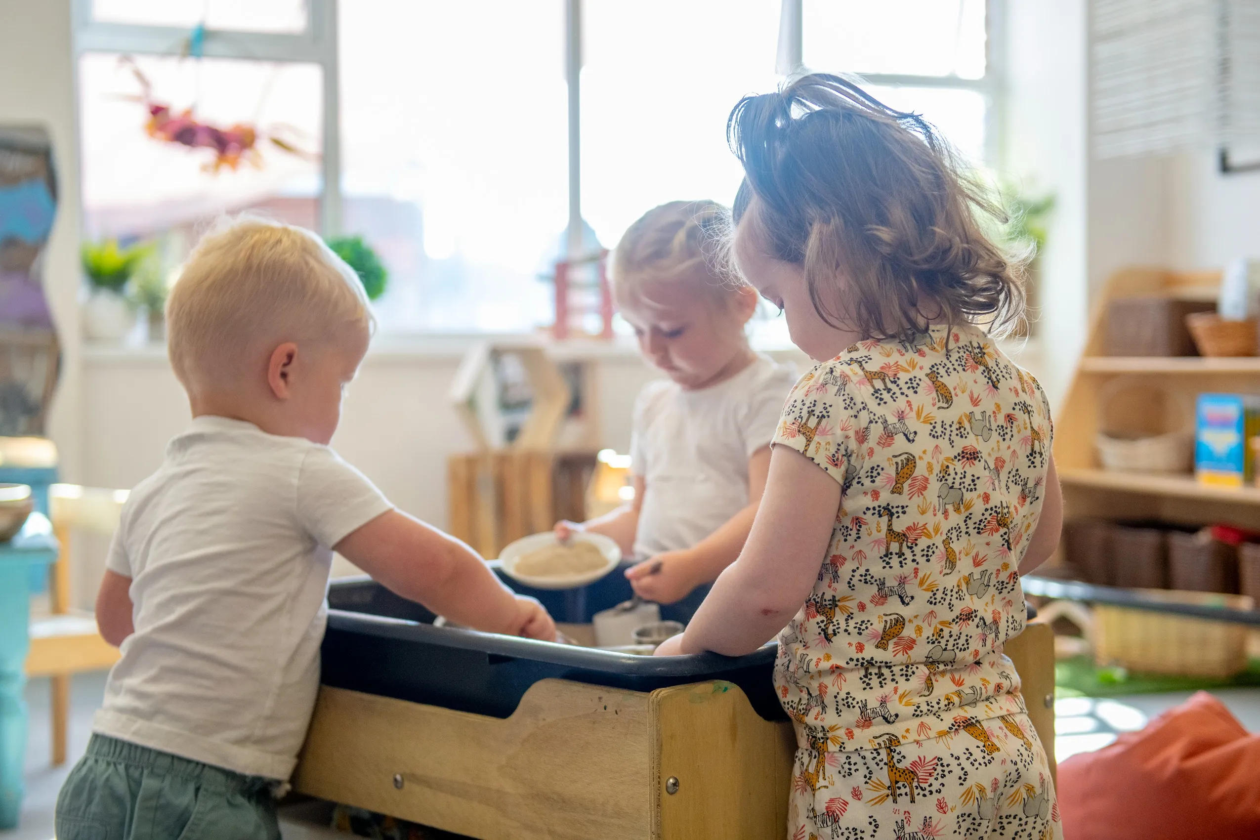 Three young children playing around a wooden sand and water table.