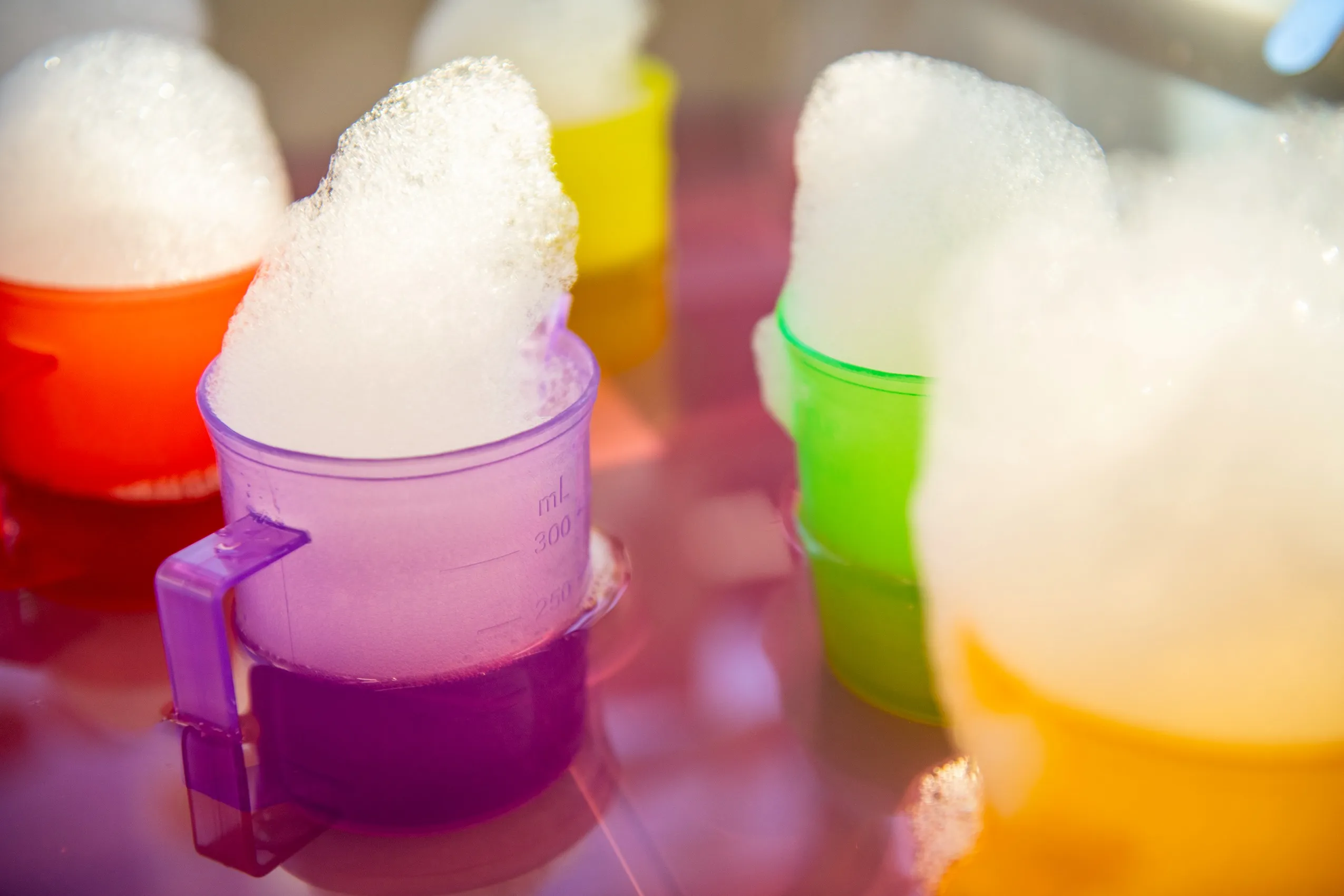 Colorful measuring cups filled with white foam, arranged in a row.