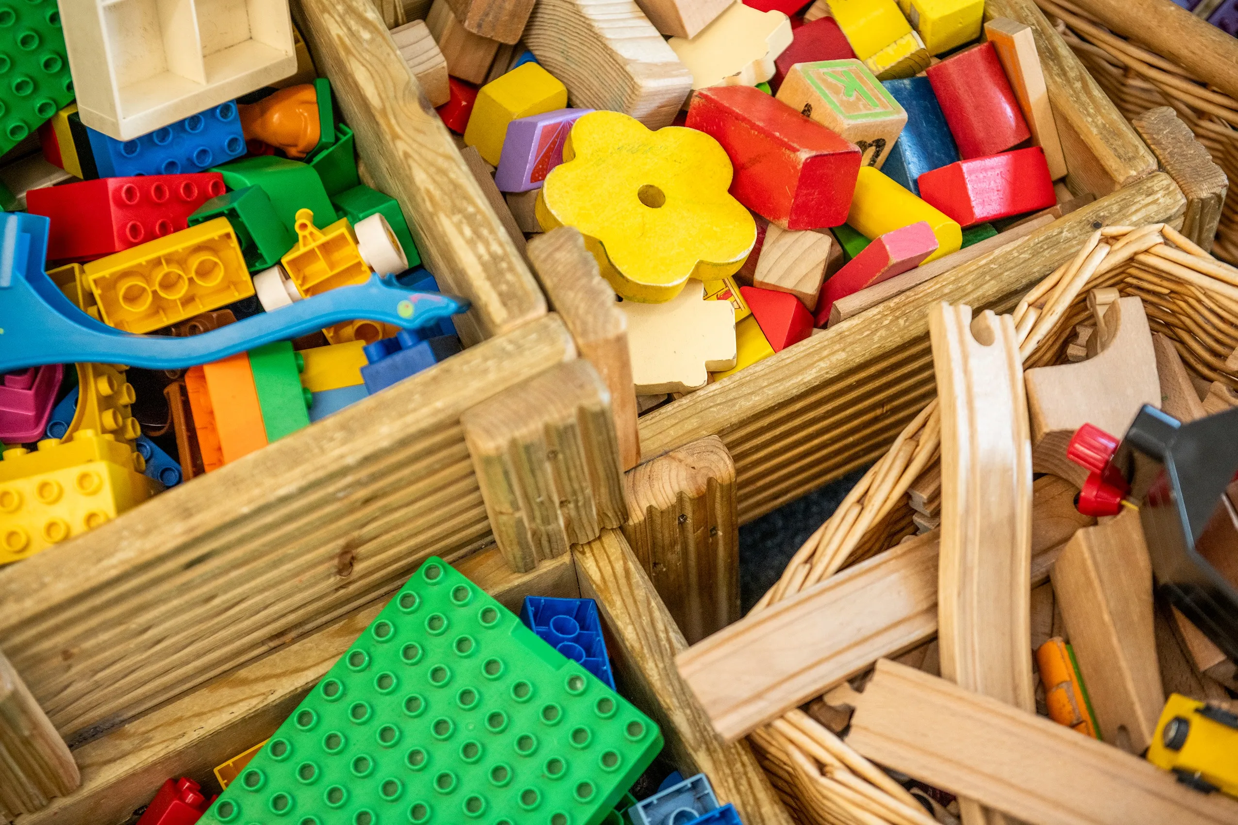 A collection of colorful building blocks and wooden toys in a container, suggesting a child's play area.