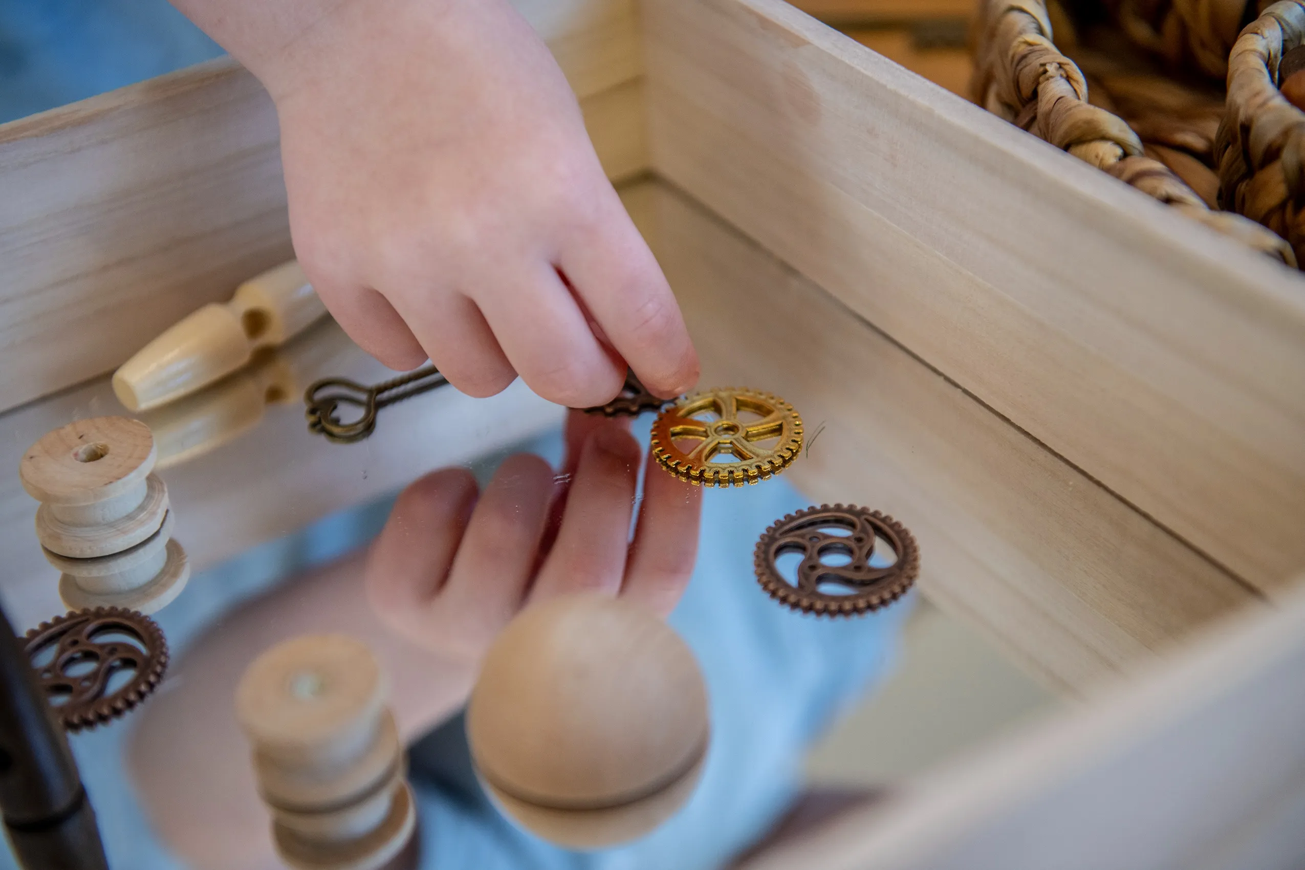 A child's hand holding a small, golden gear, suggesting a toy or educational activity.