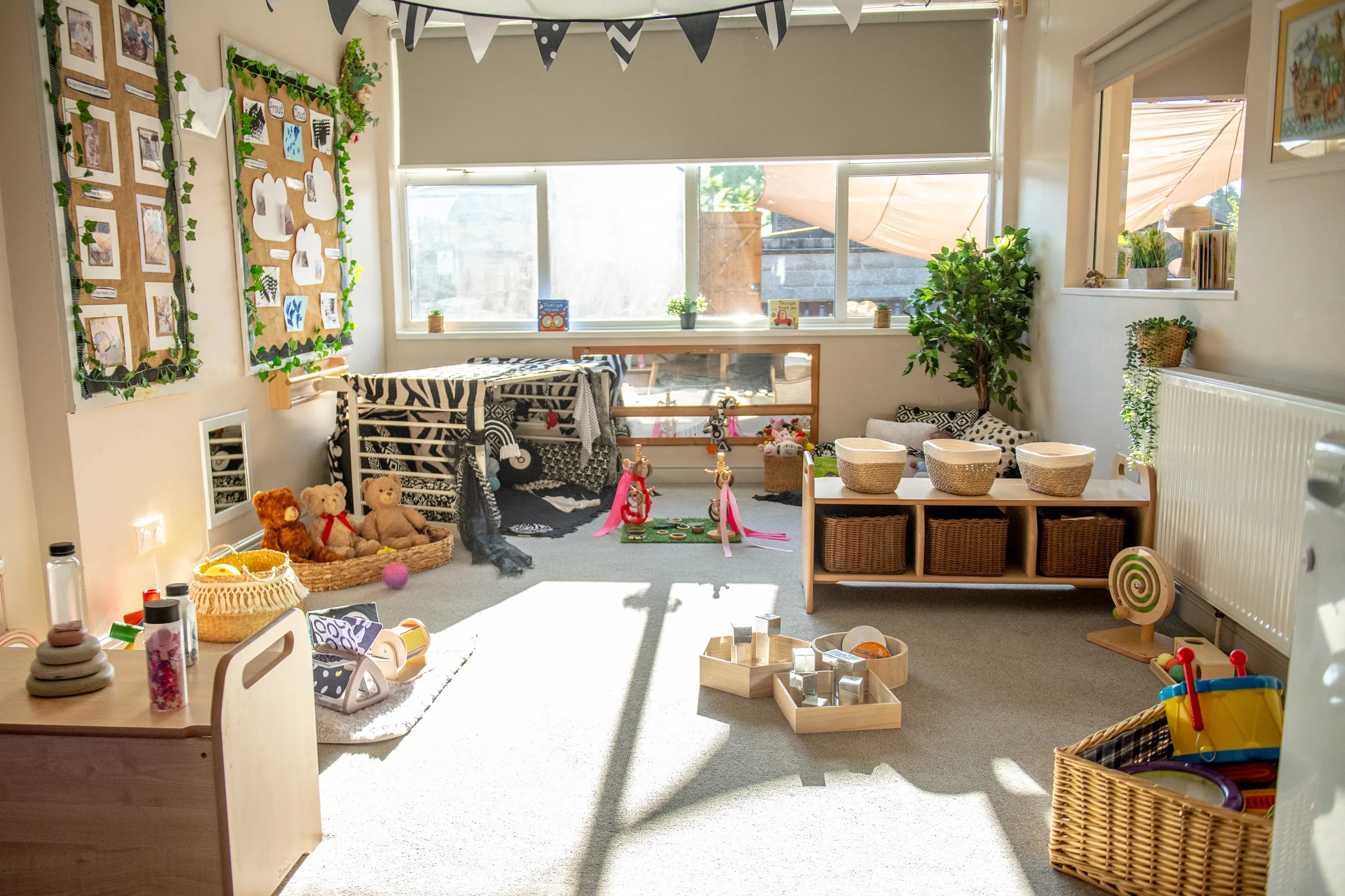 A brightly lit children's playroom with a playhouse, shelves of toys, and sensory play areas.