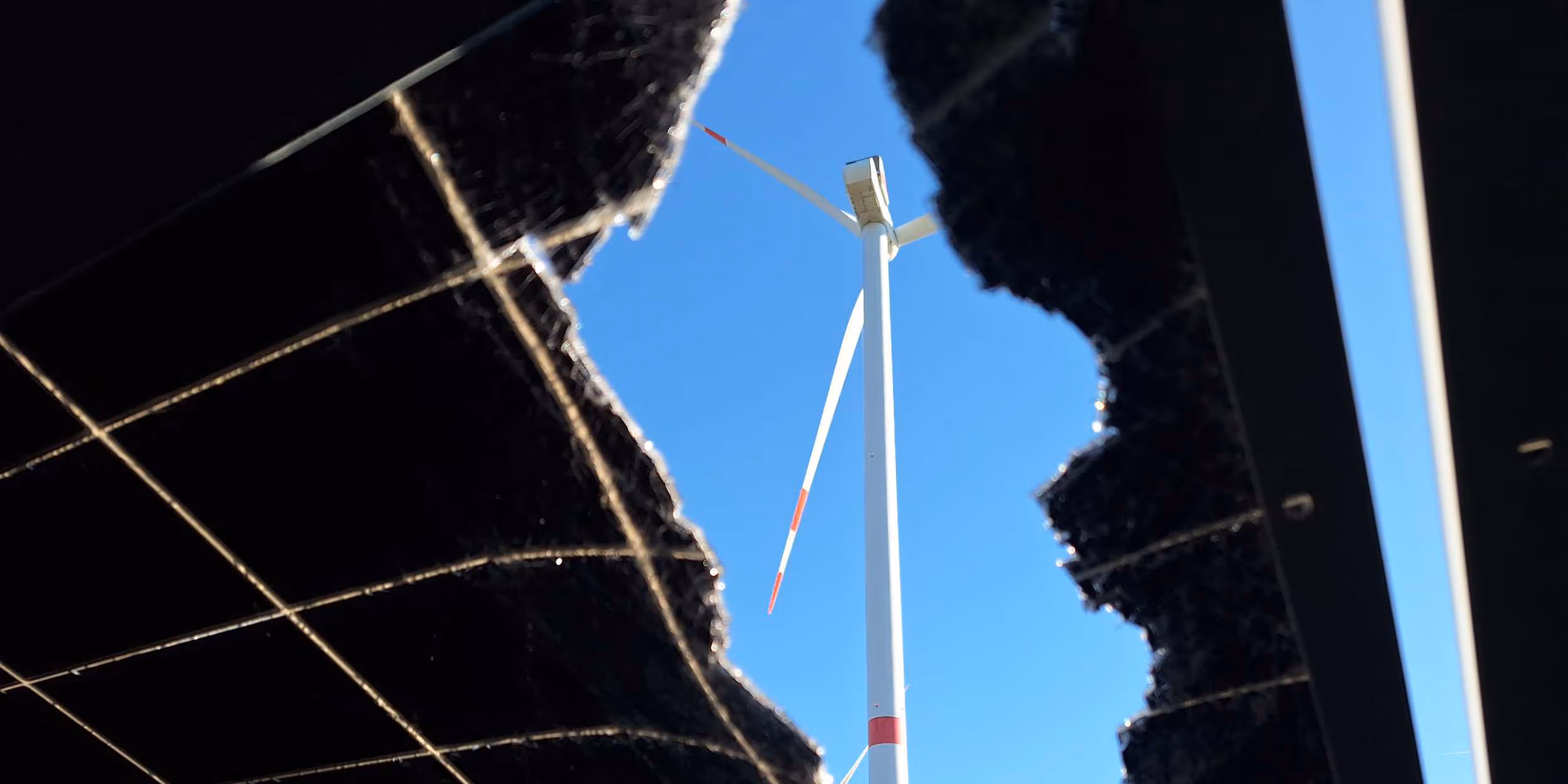 Hole in a PV module with a view of a wind turbine