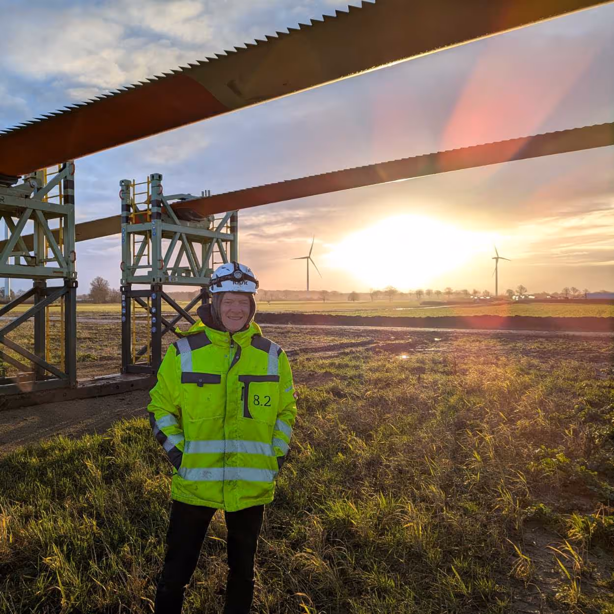 8.2 emploee daniel classen standing in front of a rotor blade of a turbine to be assembled, seems cold, sun in background, risiing