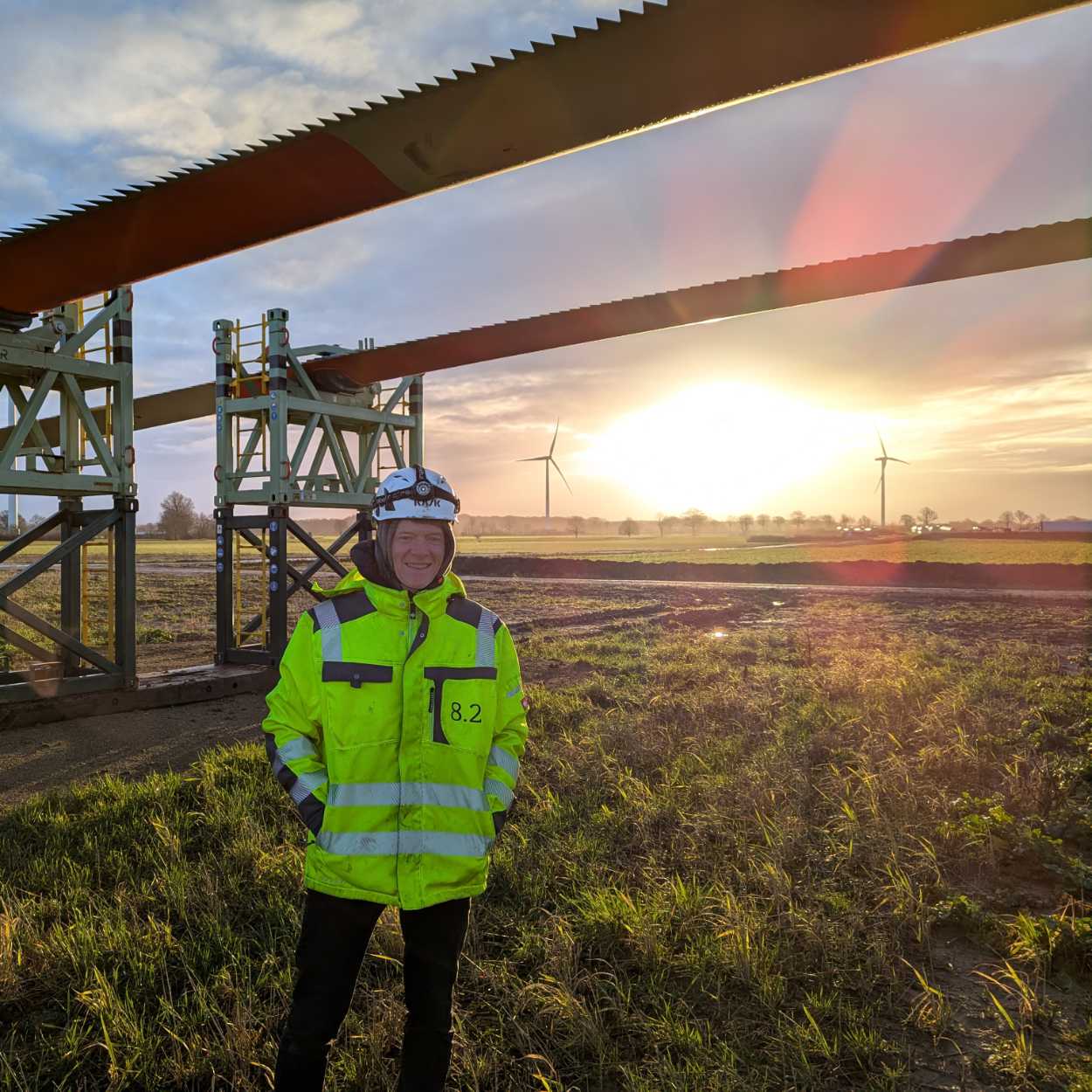 8.2 emploee daniel classen standing in front of a rotor blade of a turbine to be assembled, seems cold, sun in background, risiing