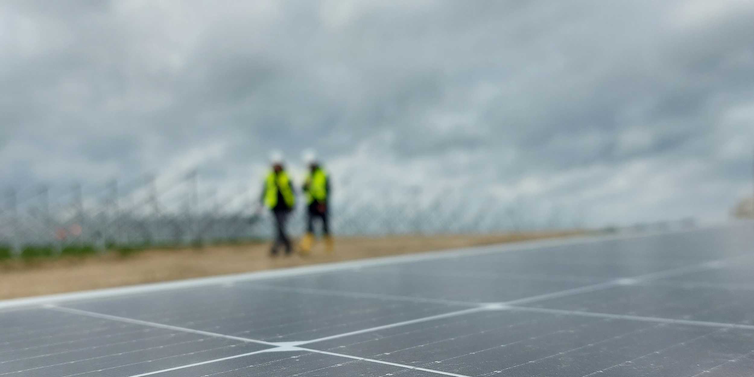 8.2 employees in background inspecting PV site with modules in front