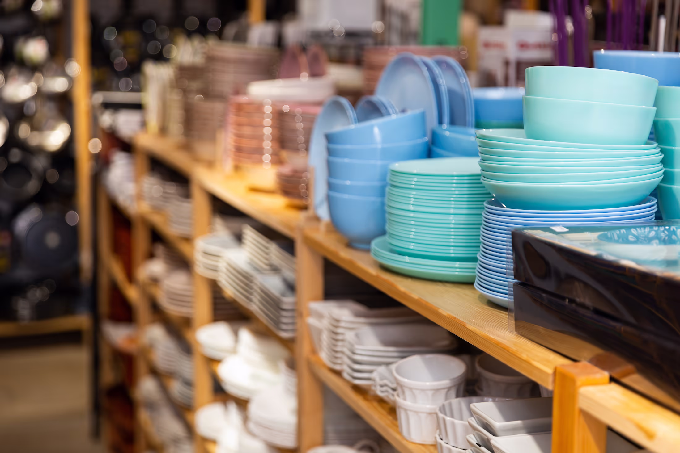 Stacks of colorful plates and bowls neatly arranged on wooden shelves in a store.