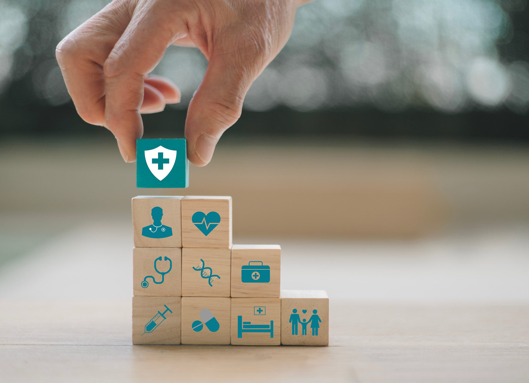 Hand stacking healthcare-themed blocks, adding one with a cross symbol on top of a pyramid.