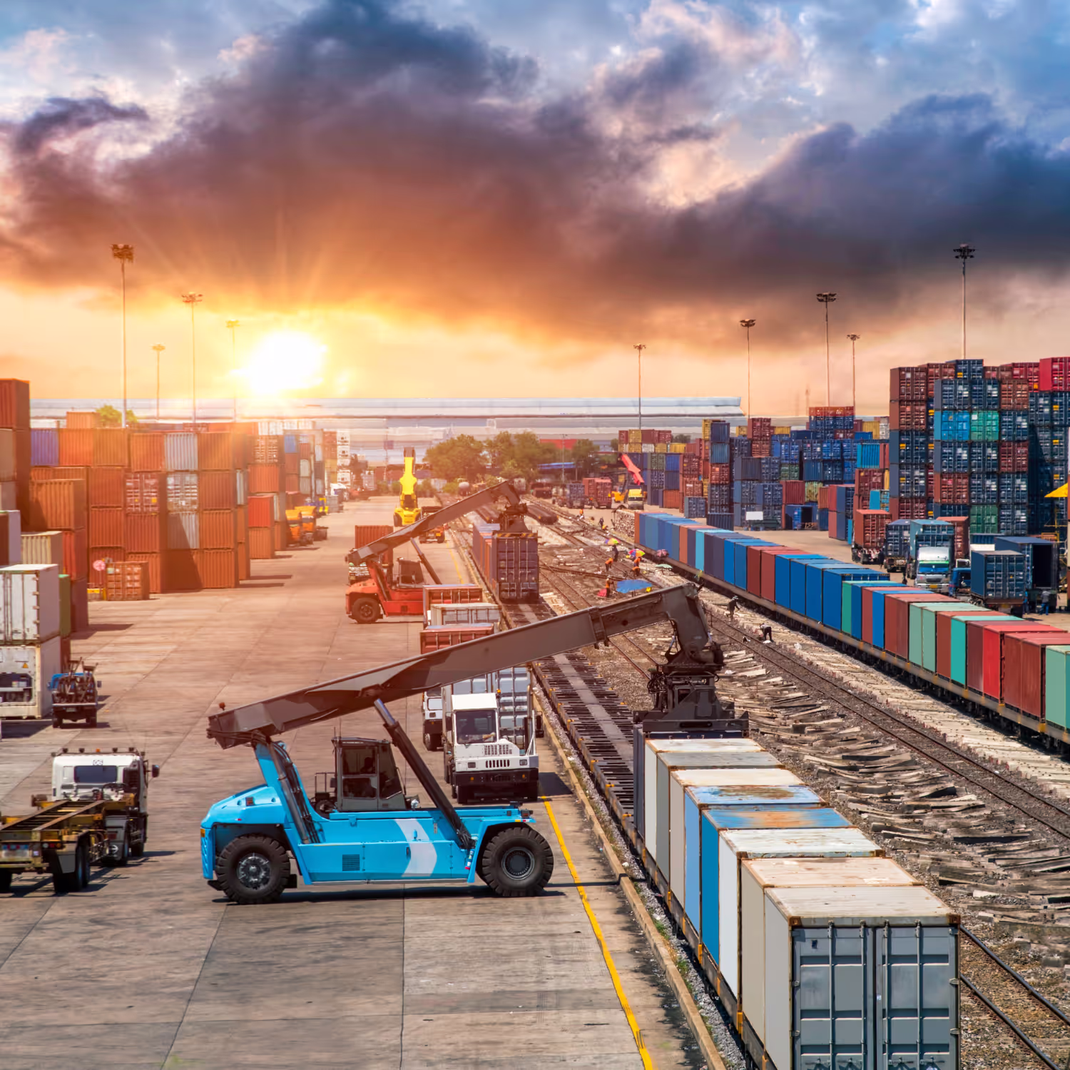 A busy freight yard with cranes loading shipping containers onto trains at sunrise.