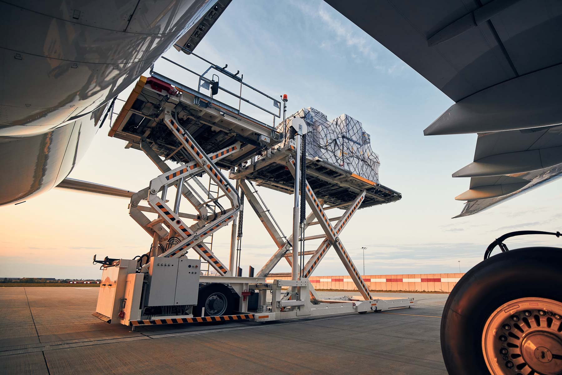 A cargo loader lifts pallets onto an airplane at the airport.