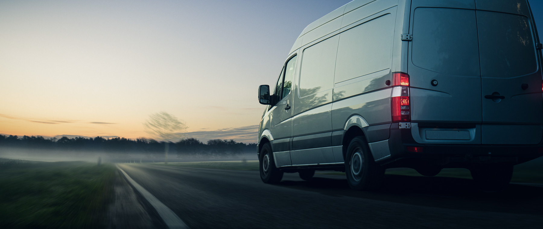 A white van drives on a rural road at sunrise.