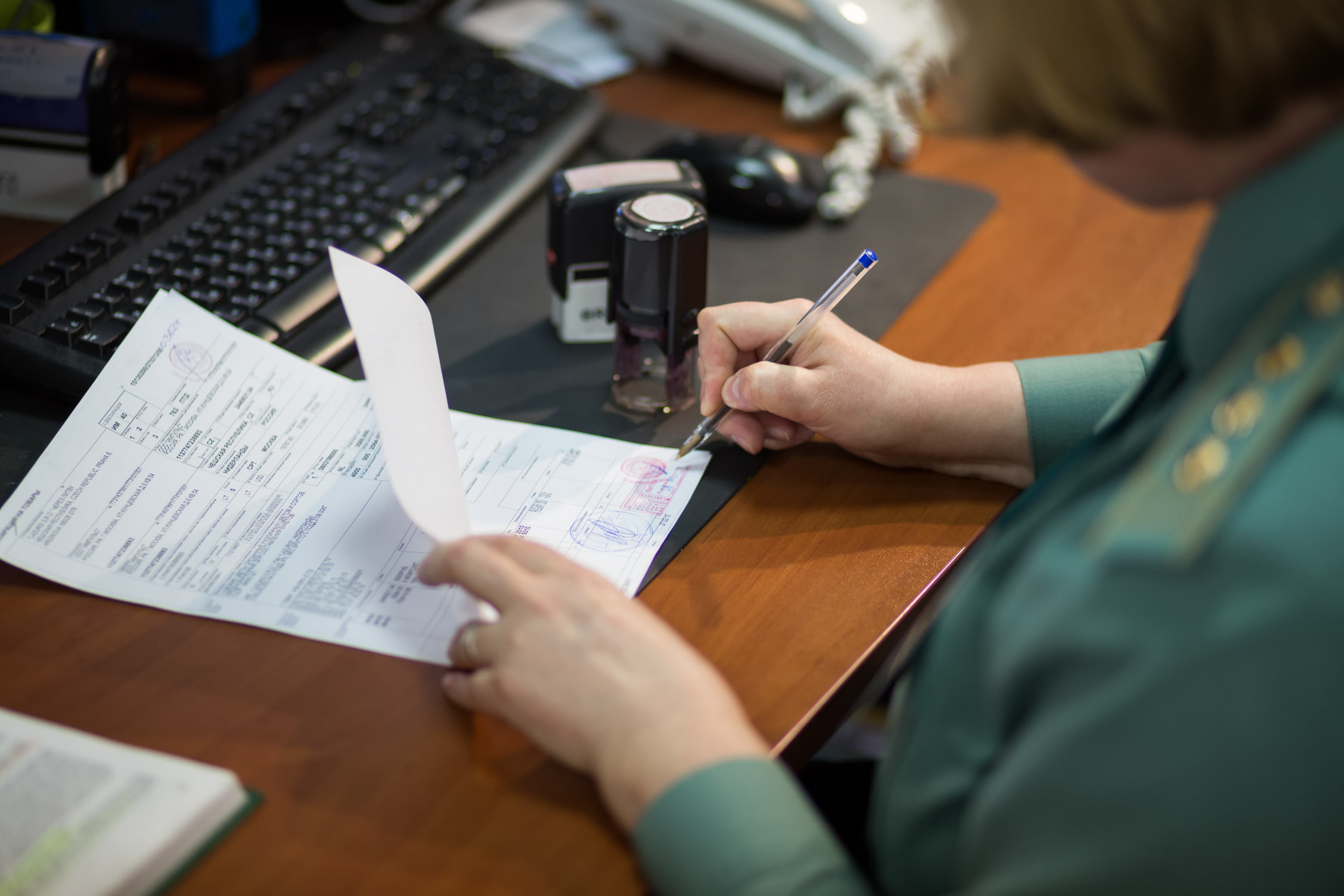 Person at a desk filling out forms with a pen and a stamp nearby.