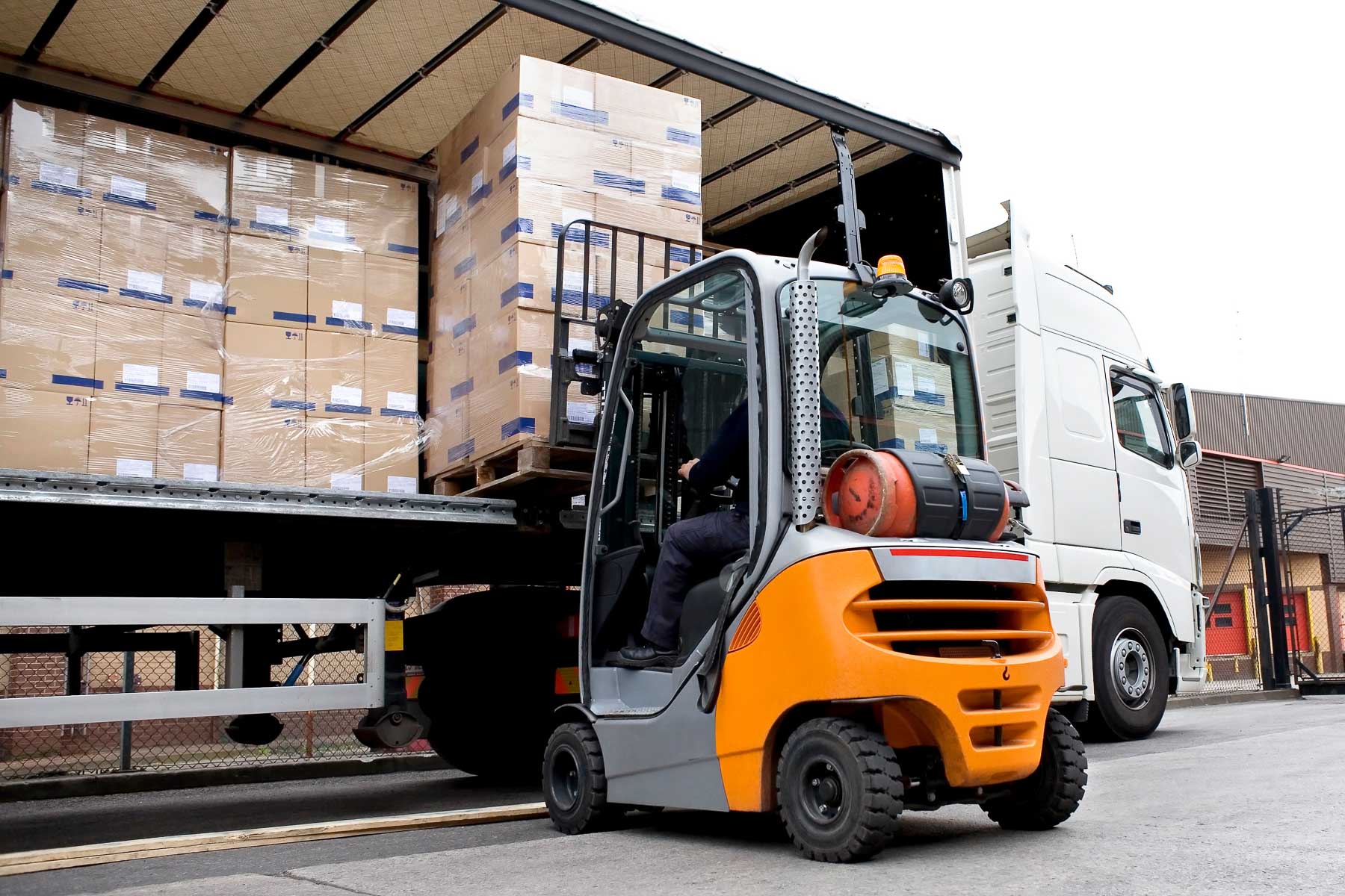 A forklift unloads large boxes from a truck at a loading dock.