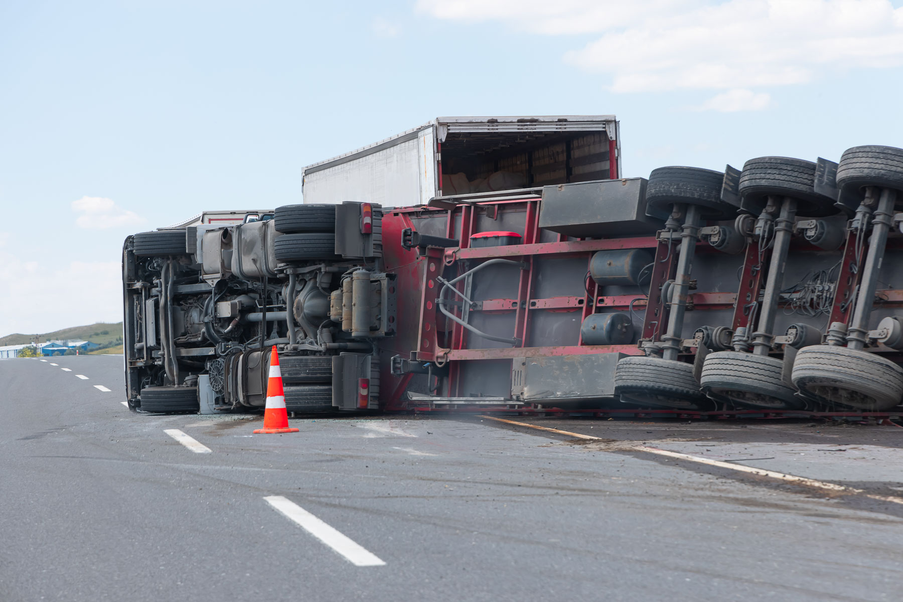 Overturned truck on highway with traffic cone placed beside it.