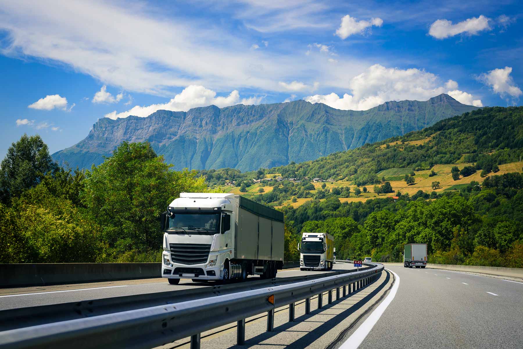 Trucks driving on a highway with mountains in the background under a blue sky.