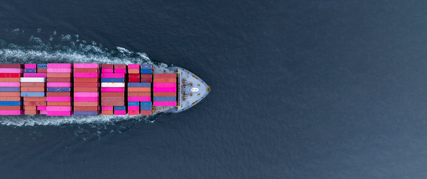 A container ship travels through the ocean, carrying multicolored containers on its deck.