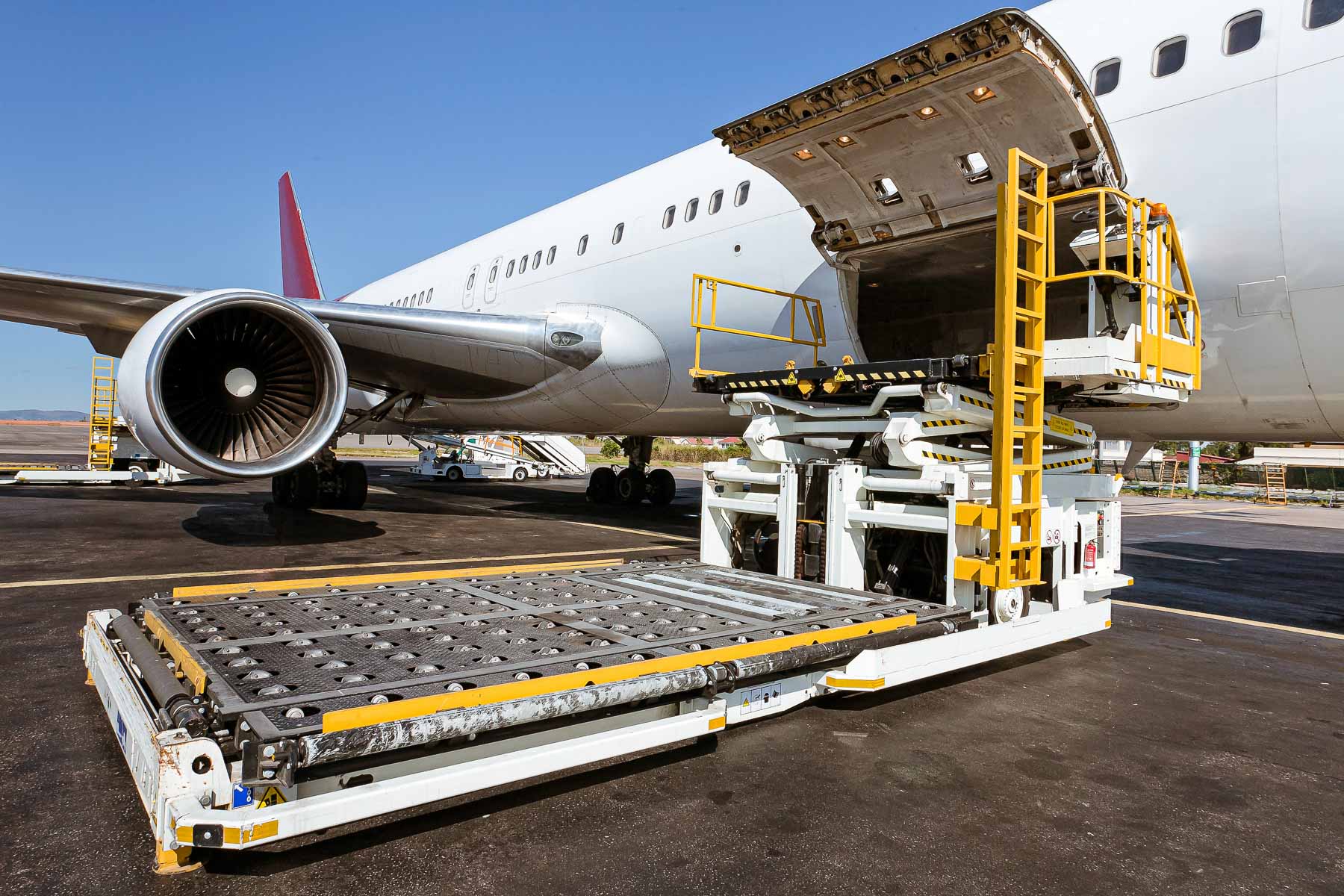 A cargo loader is positioned near an airplane, ready to load goods into the open cargo hold.