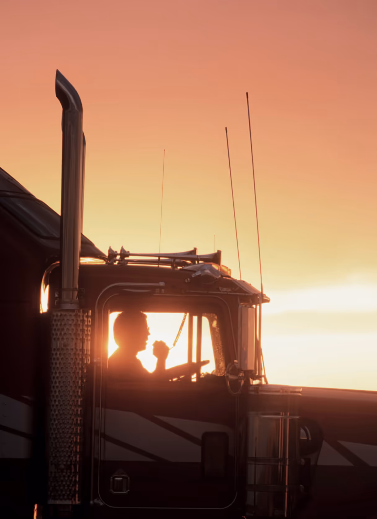 A photo of a man driving a truck at sunset