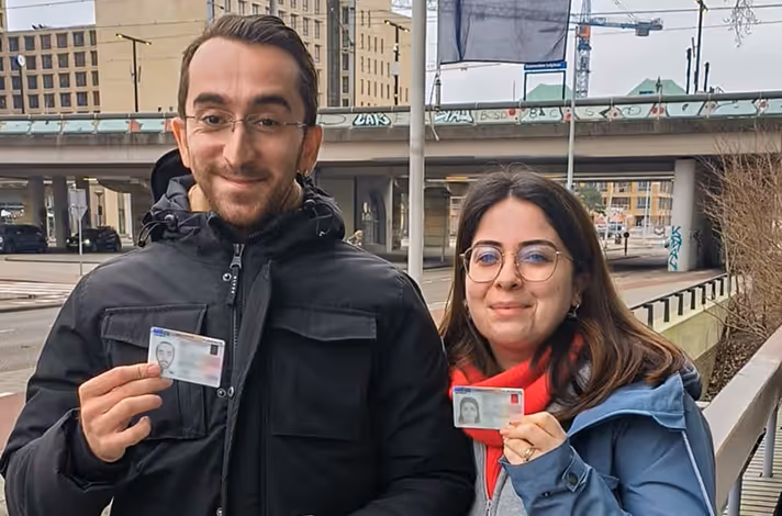 Two young people posing for a photo holding Dutch documents, happy that they got relocated to the Netherlands