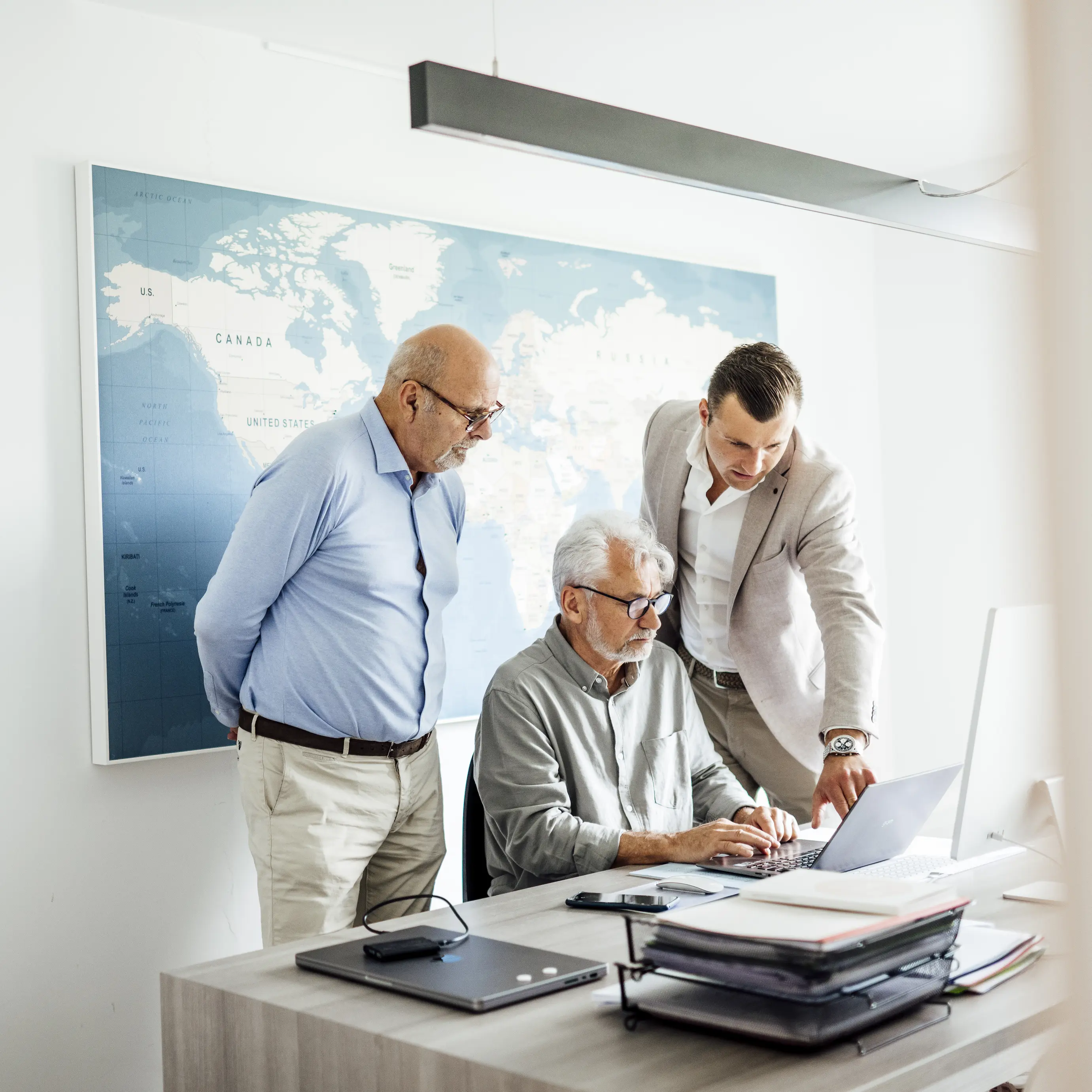 Marc, Guillaume and Anton from Fedeco Foods collaborating at the desk during a meeting, working together on a document with a large world map in the background.