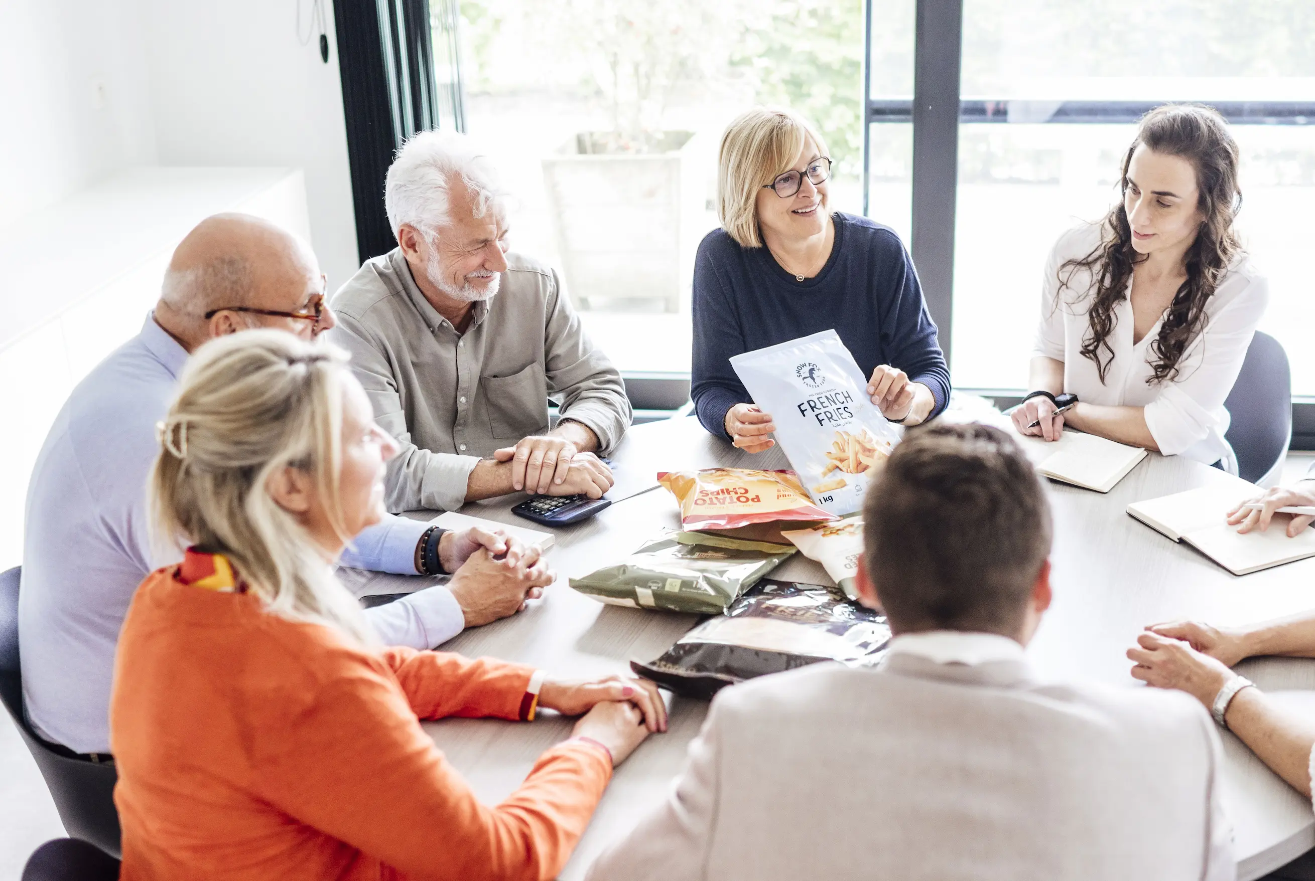 Fedeco team seated around a table discussing snack packaging, with one woman holding a bag of French fries.