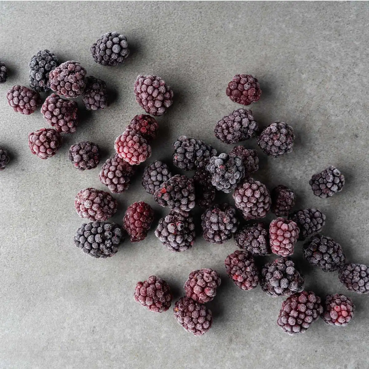 Frozen blackberries scattered on a gray textured surface.