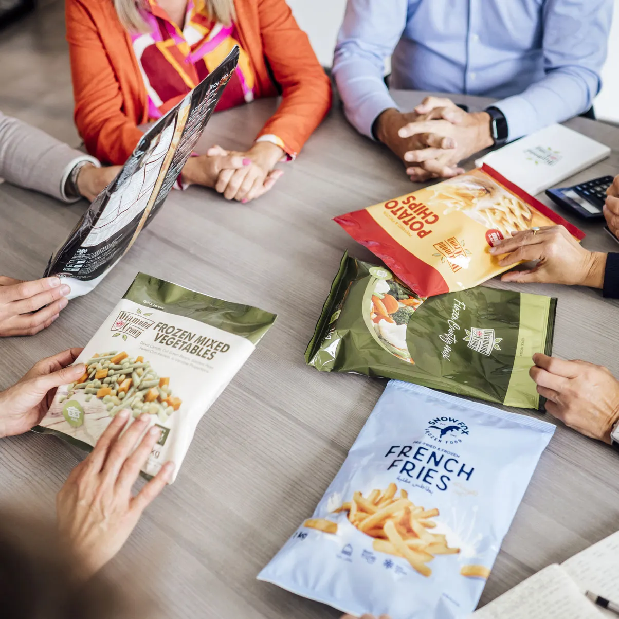 People sitting around a table holding and discussing frozen food packages of fries and mixed vegetables.