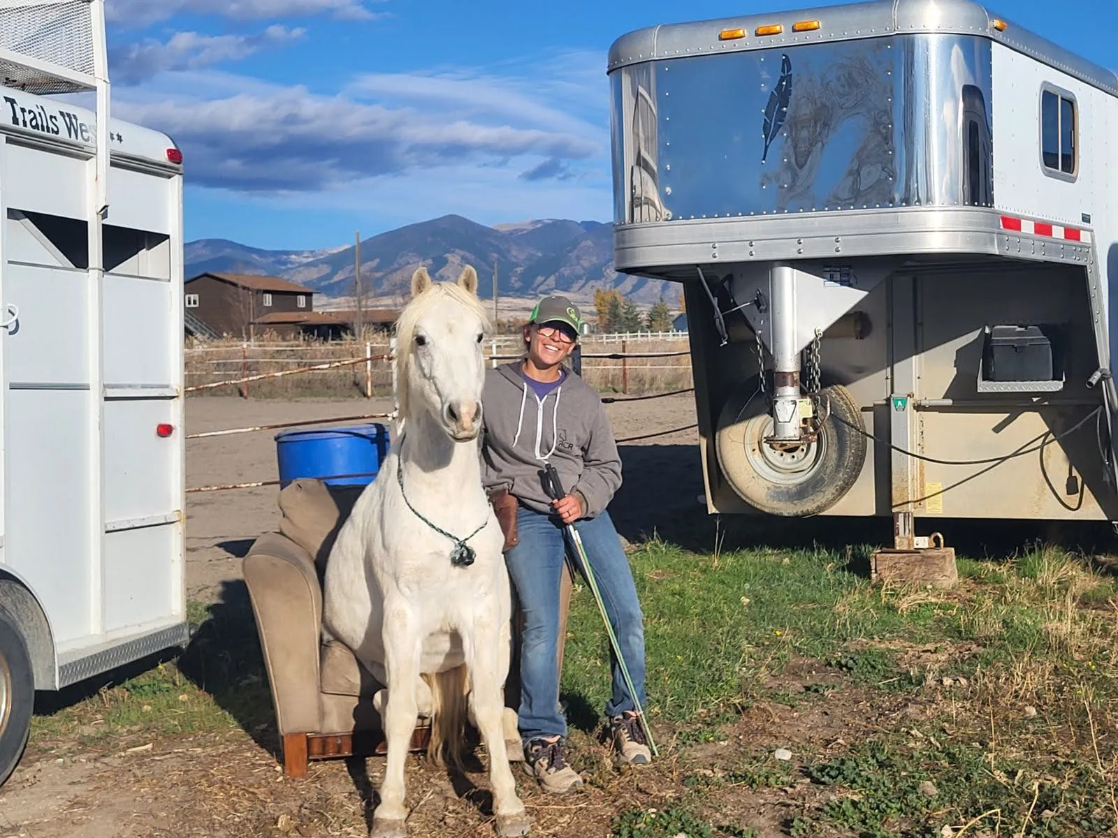 A white pony sitting down next to its smiling trainer.
