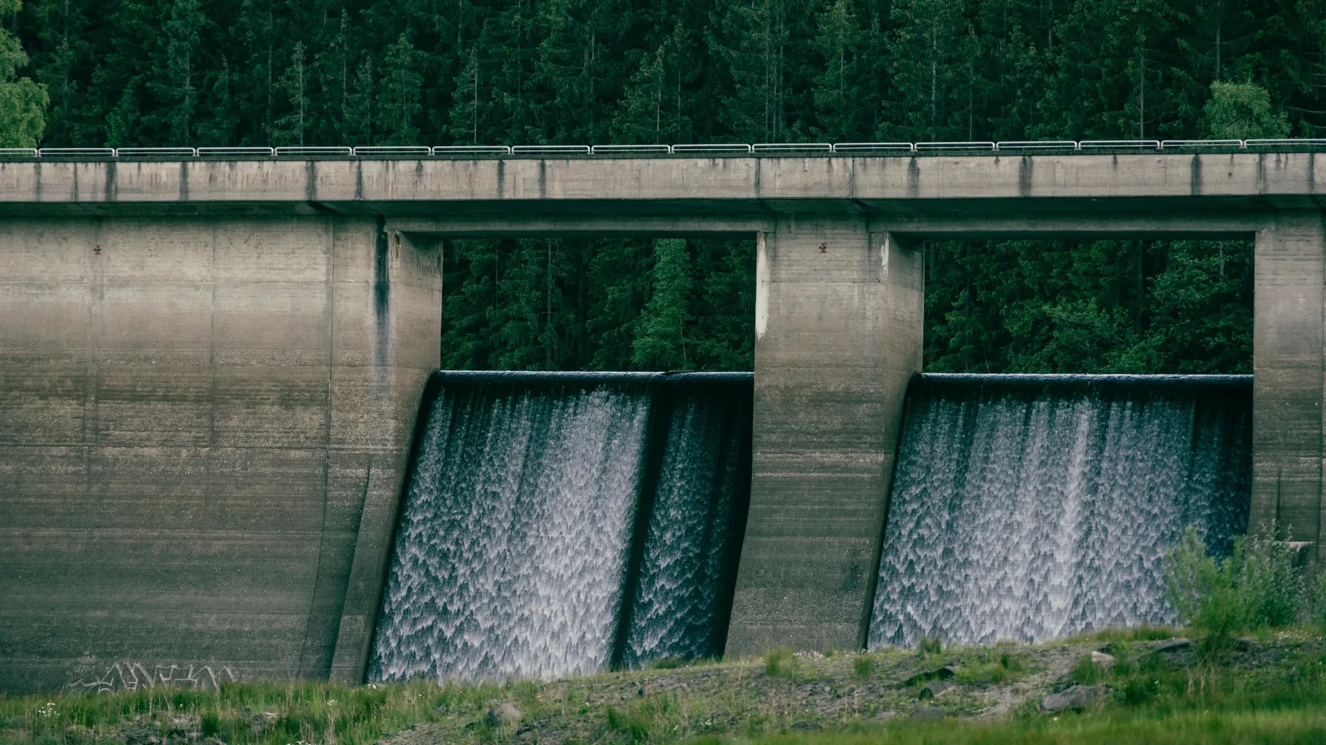 Hydropower dam with water flowing through two spillways, surrounded by forest.