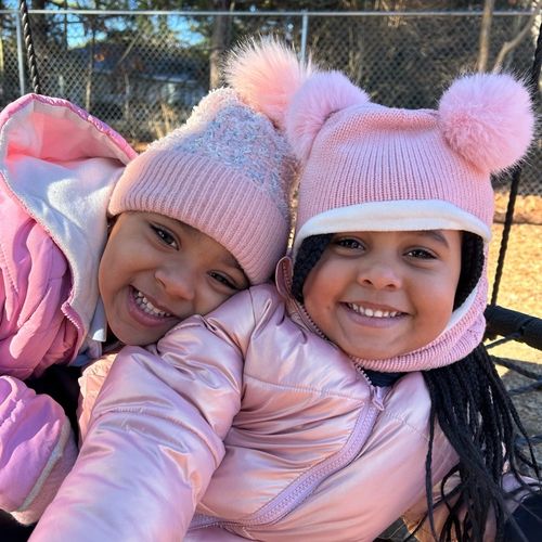Two girls are all bundled in winter clothes, smiling out on the playground